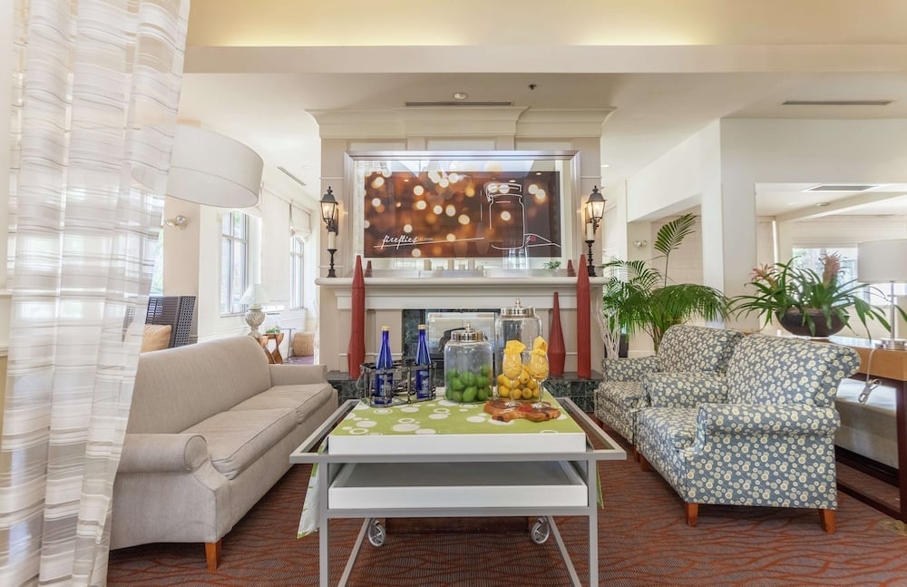 Natural light floods the welcoming lobby where geometric-patterned armchairs and fresh citrus displays create an inviting gathering space beneath exposed wooden beams.