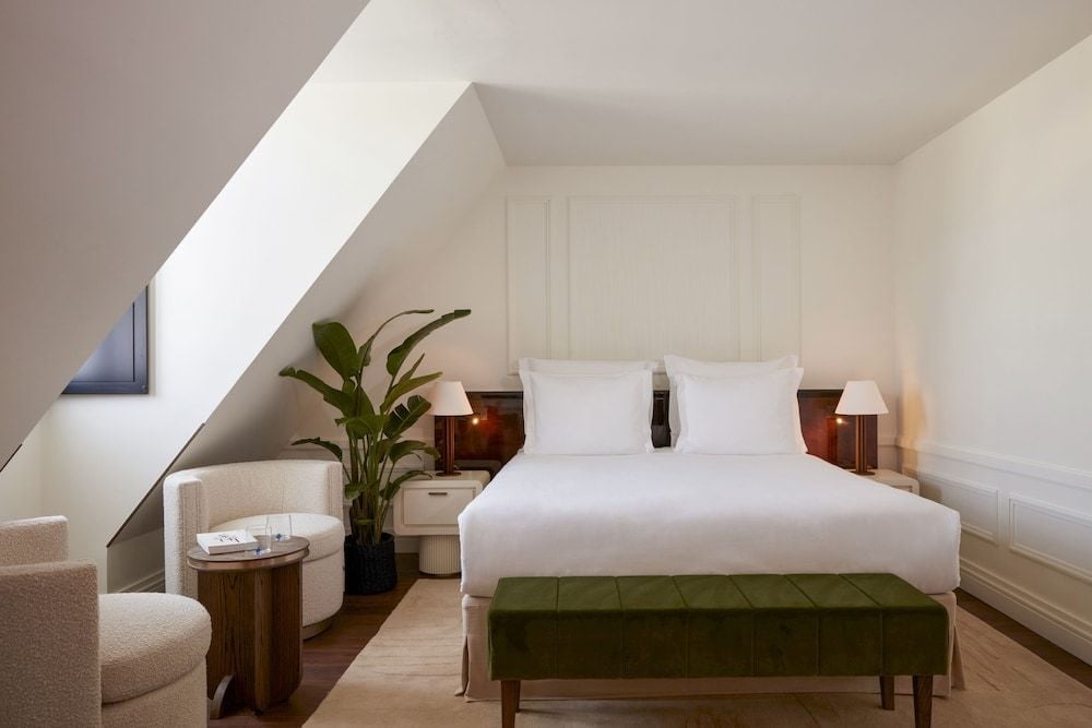 Crisp white linens contrast beautifully with emerald velvet and warm wood accents in this intimate attic suite, where exposed beams frame peaceful moments.