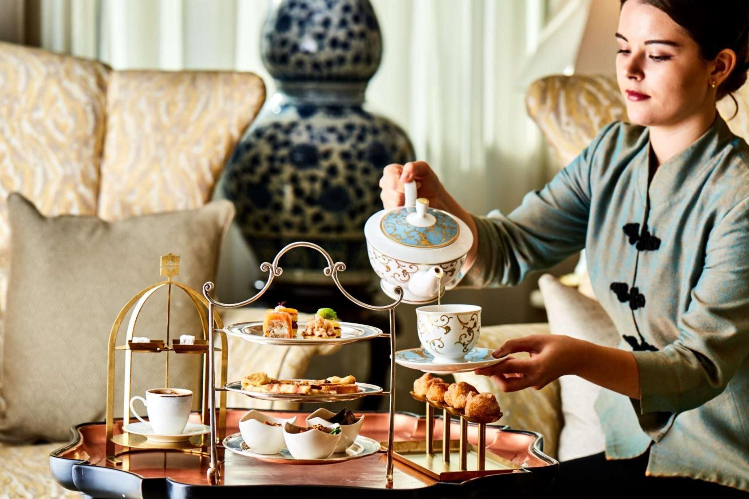 Delicate bone china and golden tiered stands create an intimate afternoon tea ritual, where warm light dances across ornate teacups in plush surroundings.