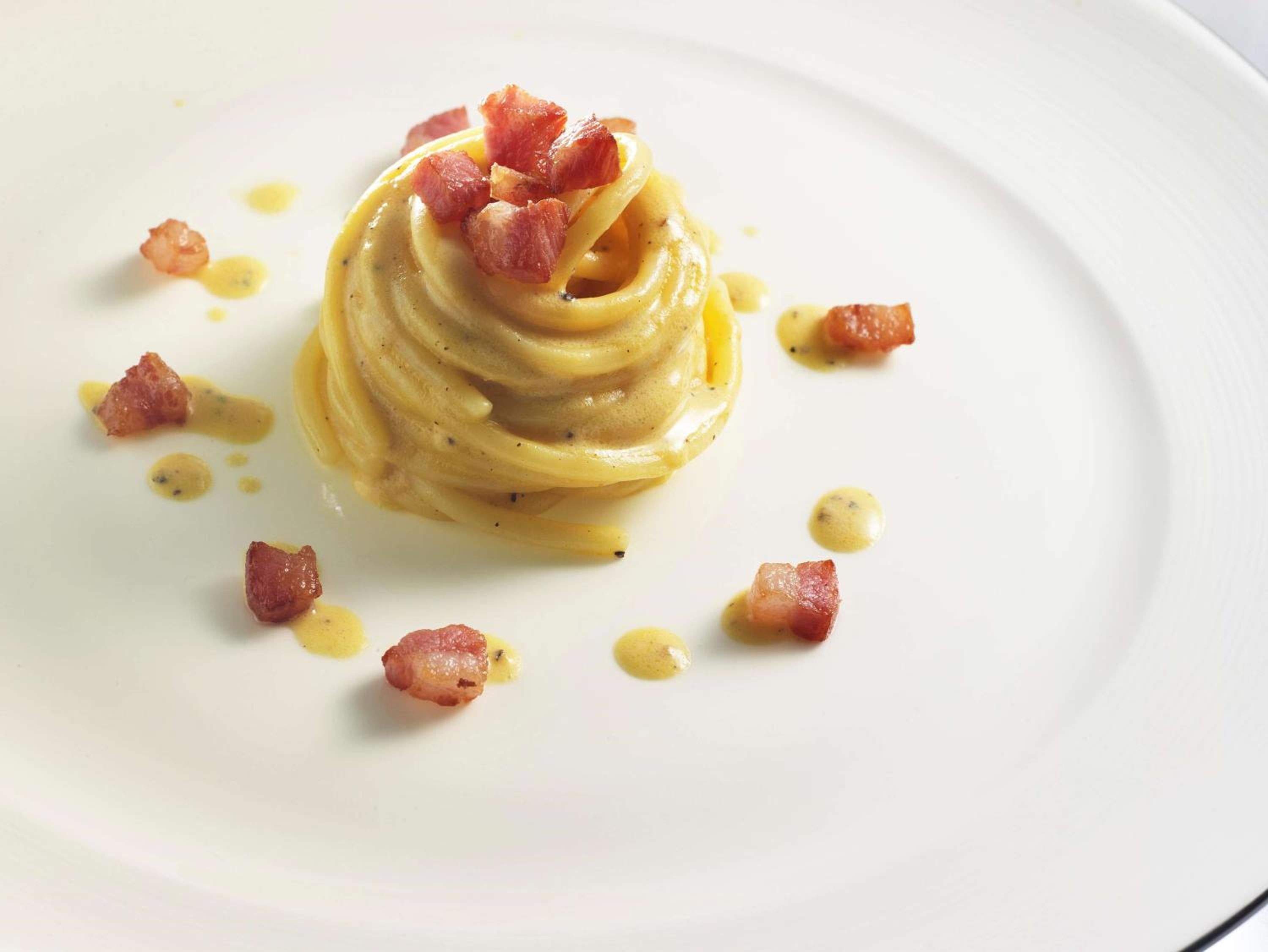 Delicate spaghetti twirls into an artistic nest, crowned with crispy pancetta and dotted with golden olive oil—Italian precision meets Japanese presentation mastery.