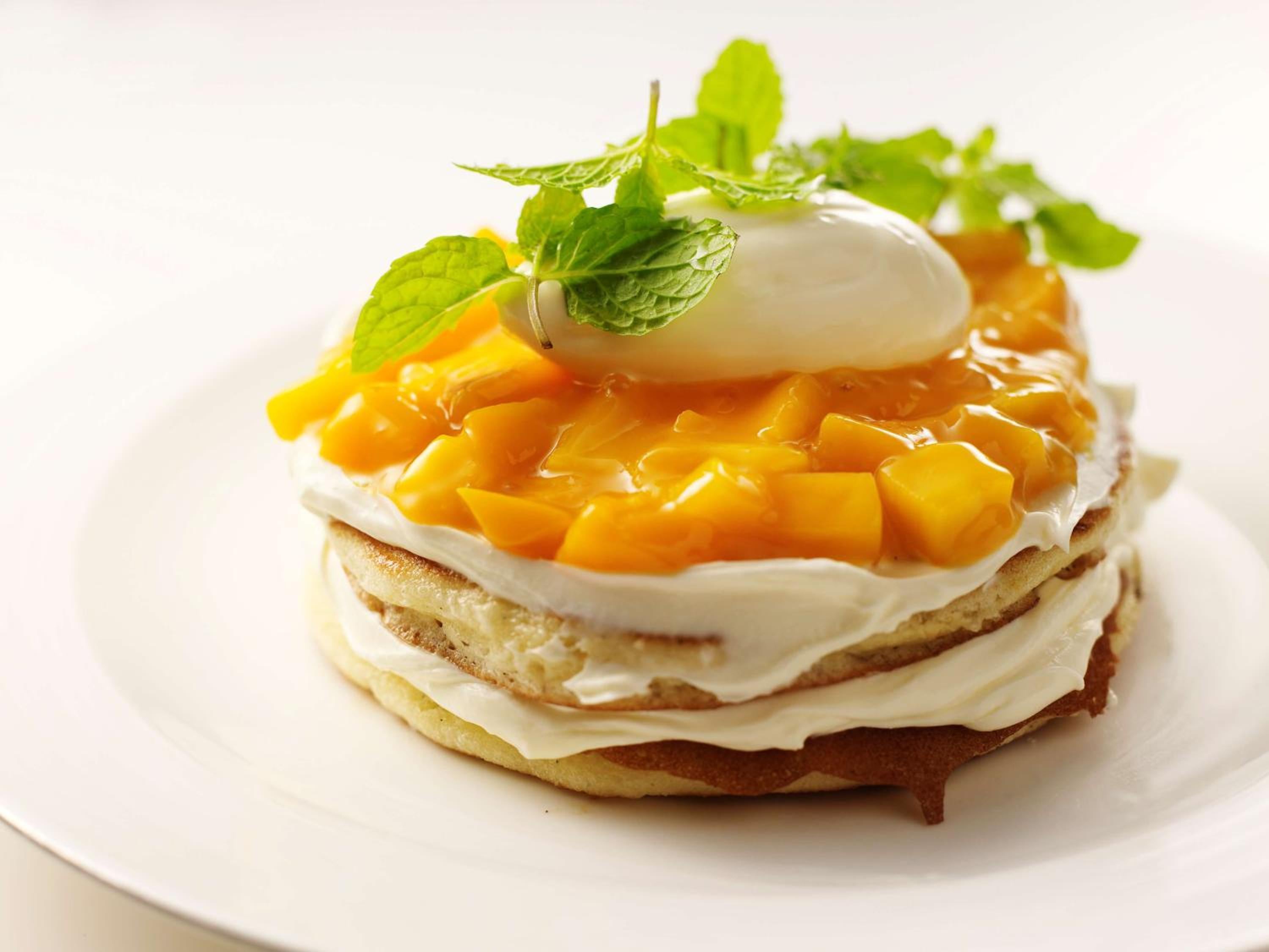 Delicate layers of sponge cake crowned with golden mango pieces and fresh mint create an artful dessert that exemplifies the hotel's refined culinary attention to detail.