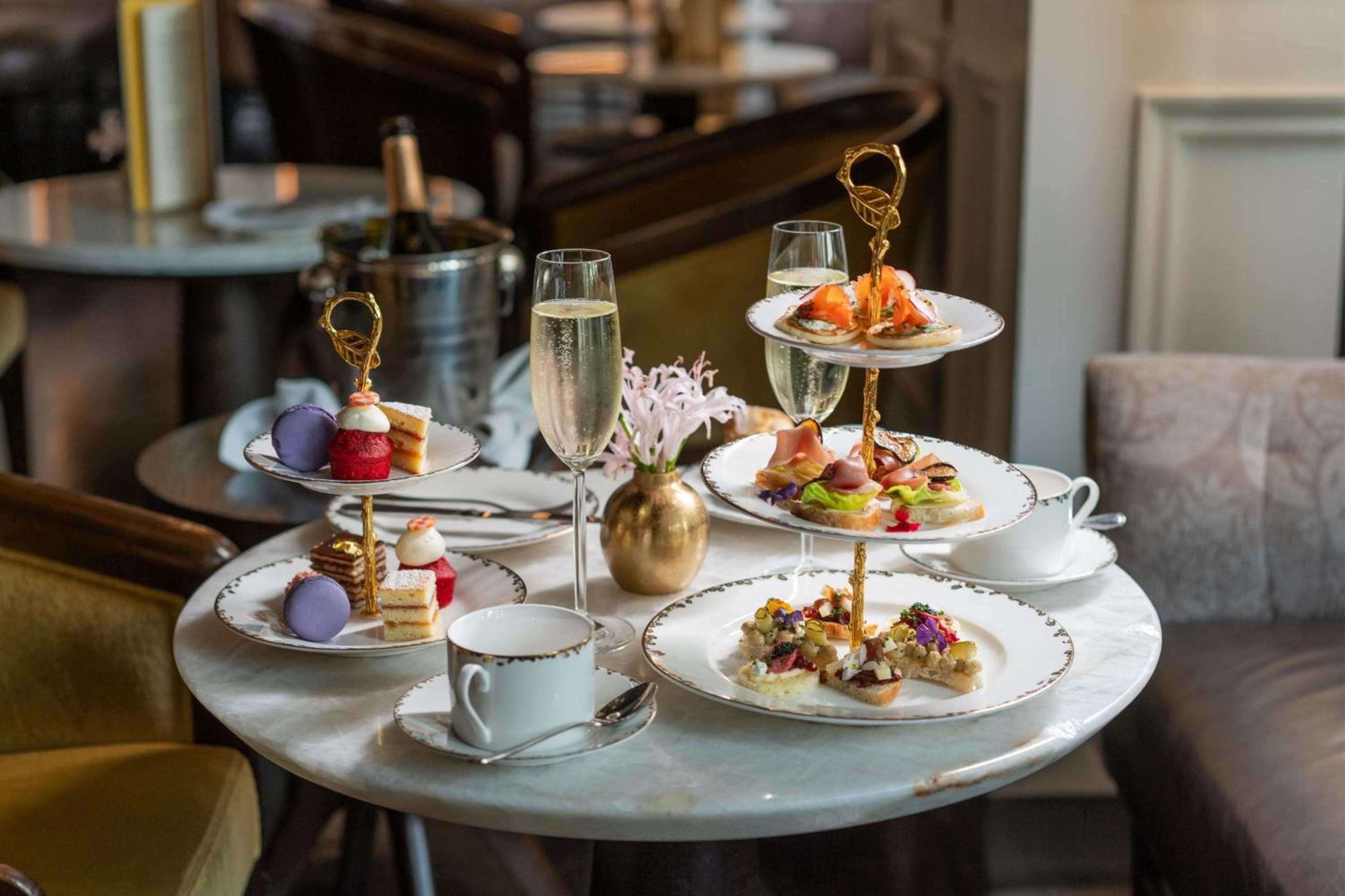 Afternoon tea arrives on gilded stands with champagne flutes catching natural light, while delicate canapés and macarons create an intimate ritual of refined indulgence.