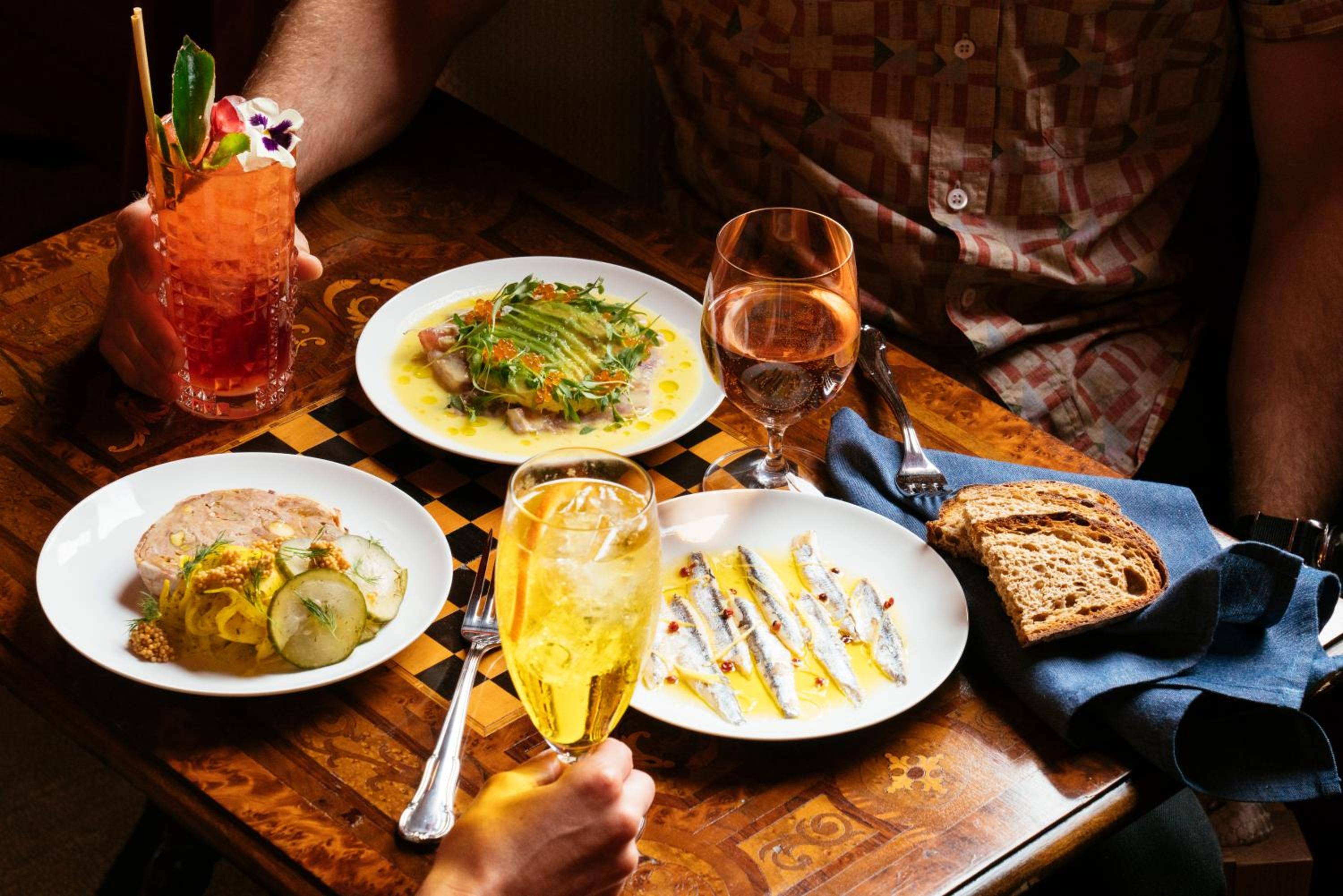 Artfully plated dishes and craft cocktails create an intimate dining tableau on rich wood tables, where culinary artistry meets convivial atmosphere.