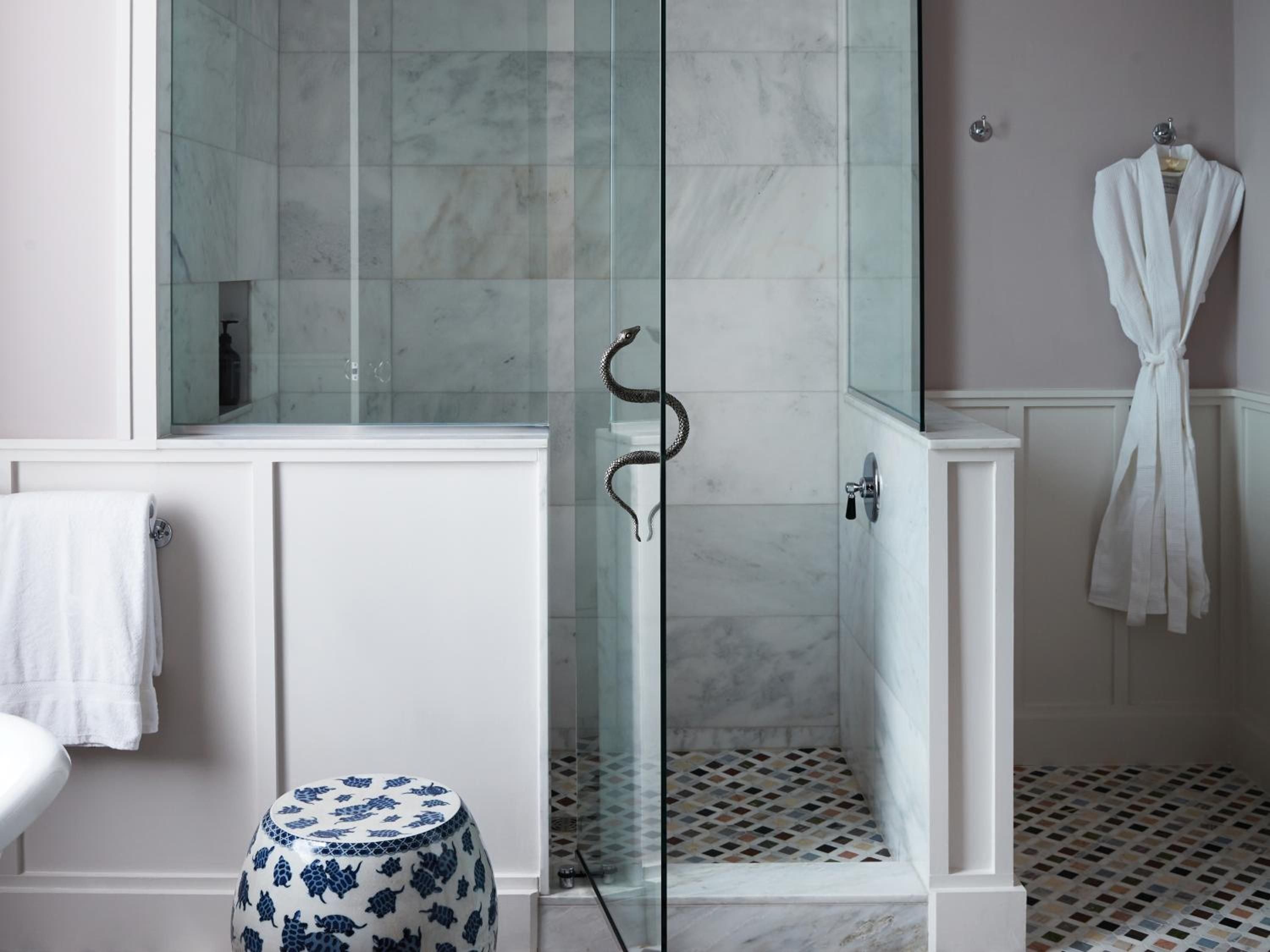 Marble-lined shower enclosures frame an unexpected serpentine sculpture, where contemporary luxury meets artistic whimsy on geometric mosaic floors.