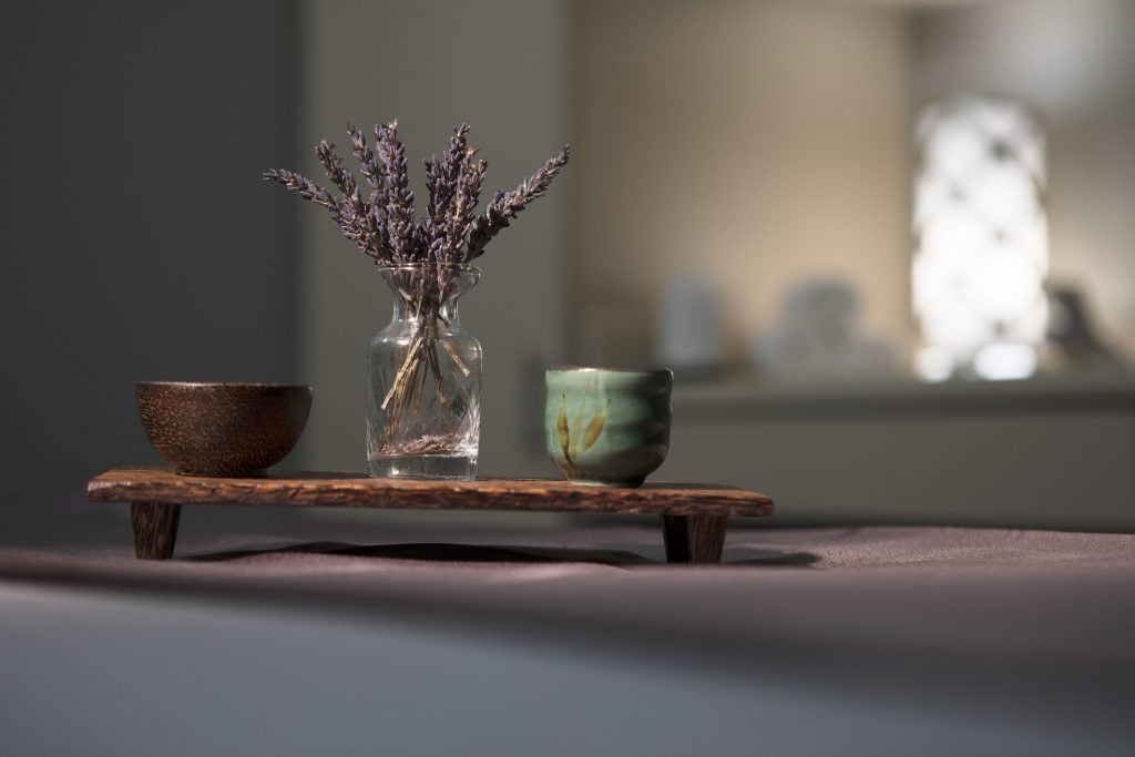 Dried lavender springs from a crystal vase on weathered wood, flanked by handcrafted ceramics that speak to The Ballantyne's artisanal attention to tranquil details.