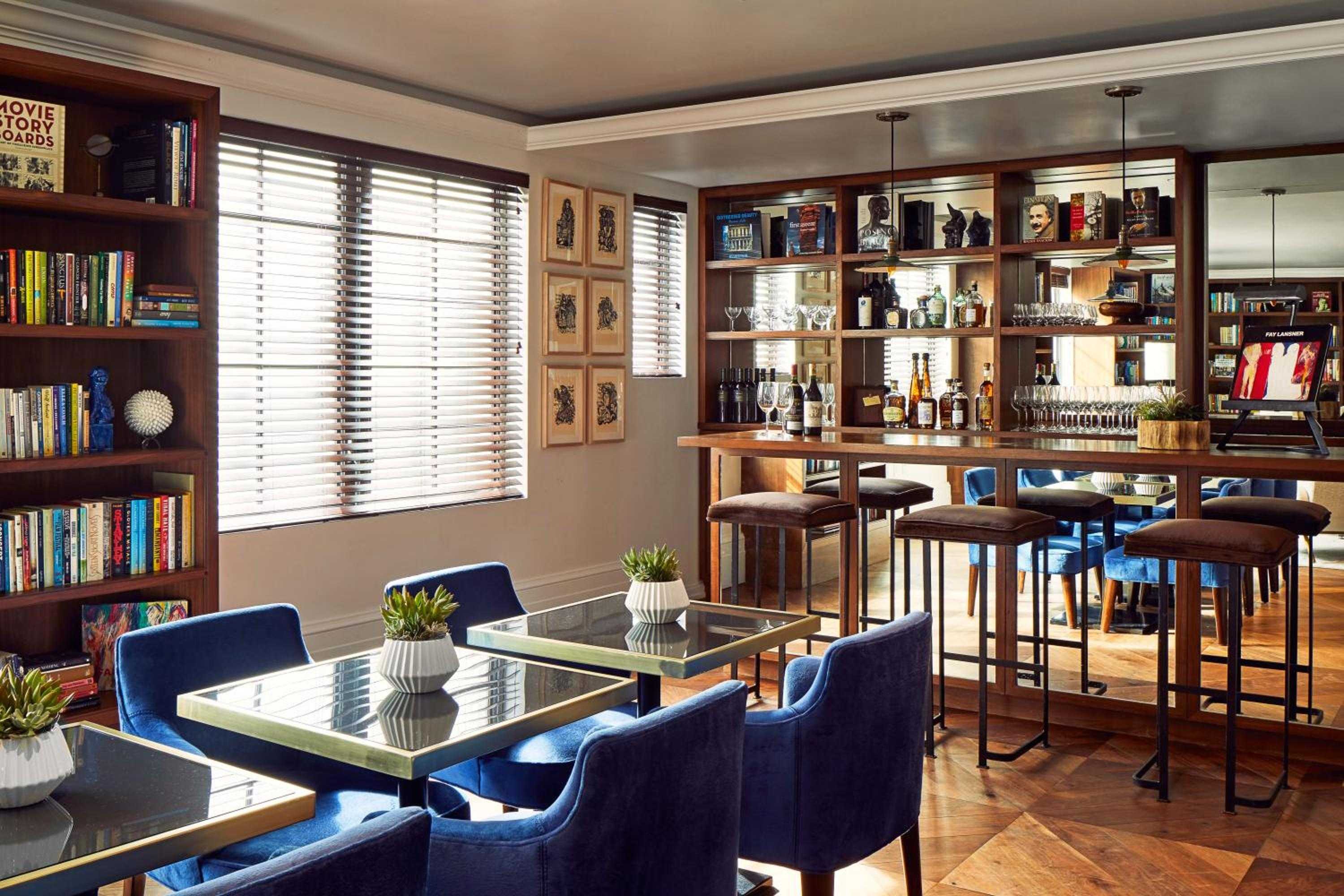 Rich walnut shelving frames vintage spirits and literary treasures, while navy velvet chairs invite lingering conversations over craft cocktails in this sophisticated reading room.