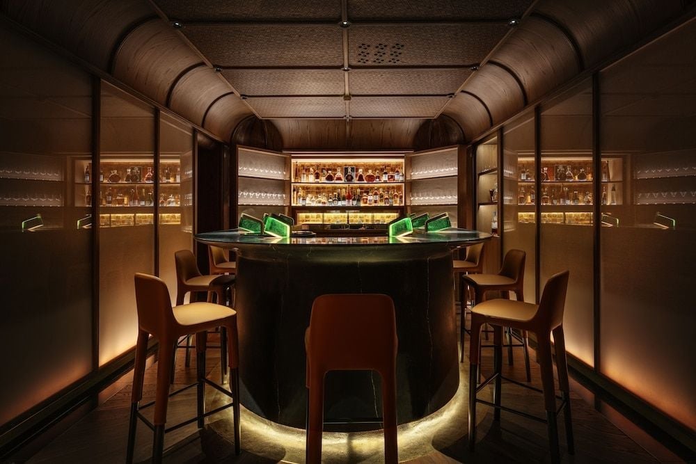 Amber light bathes this intimate circular bar where leather stools invite lingering over rare spirits displayed in illuminated cases like precious jewels.