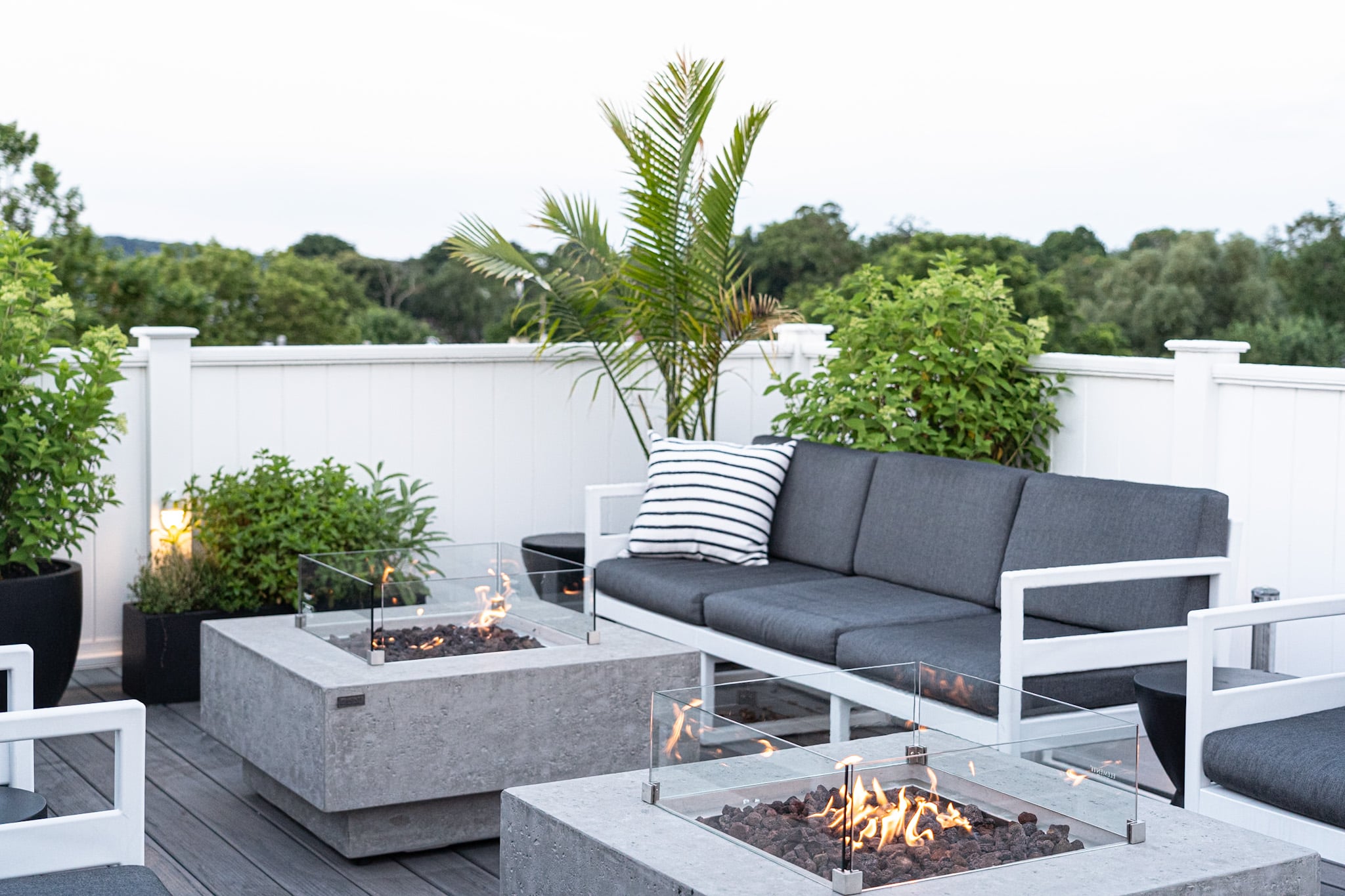 Modern fire features warm the evening air on this sophisticated rooftop terrace, where sleek seating and tropical plantings create an urban oasis above the treeline.