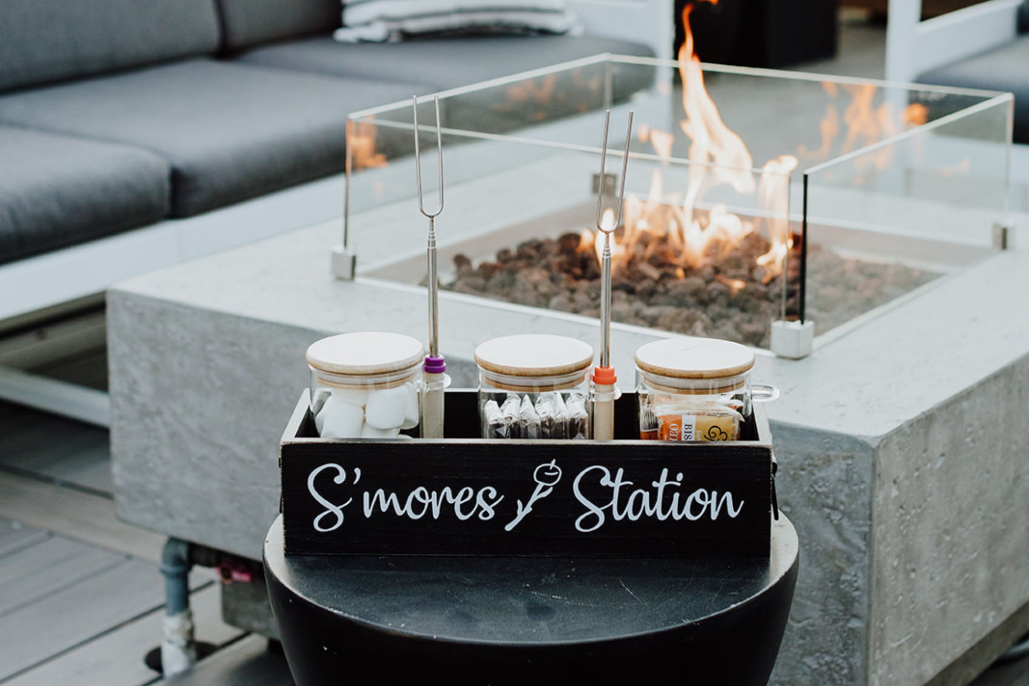 Roasting marshmallows becomes an elegant affair with a curated s'mores station beside the sleek glass-enclosed fire pit, where flames dance against modern concrete.