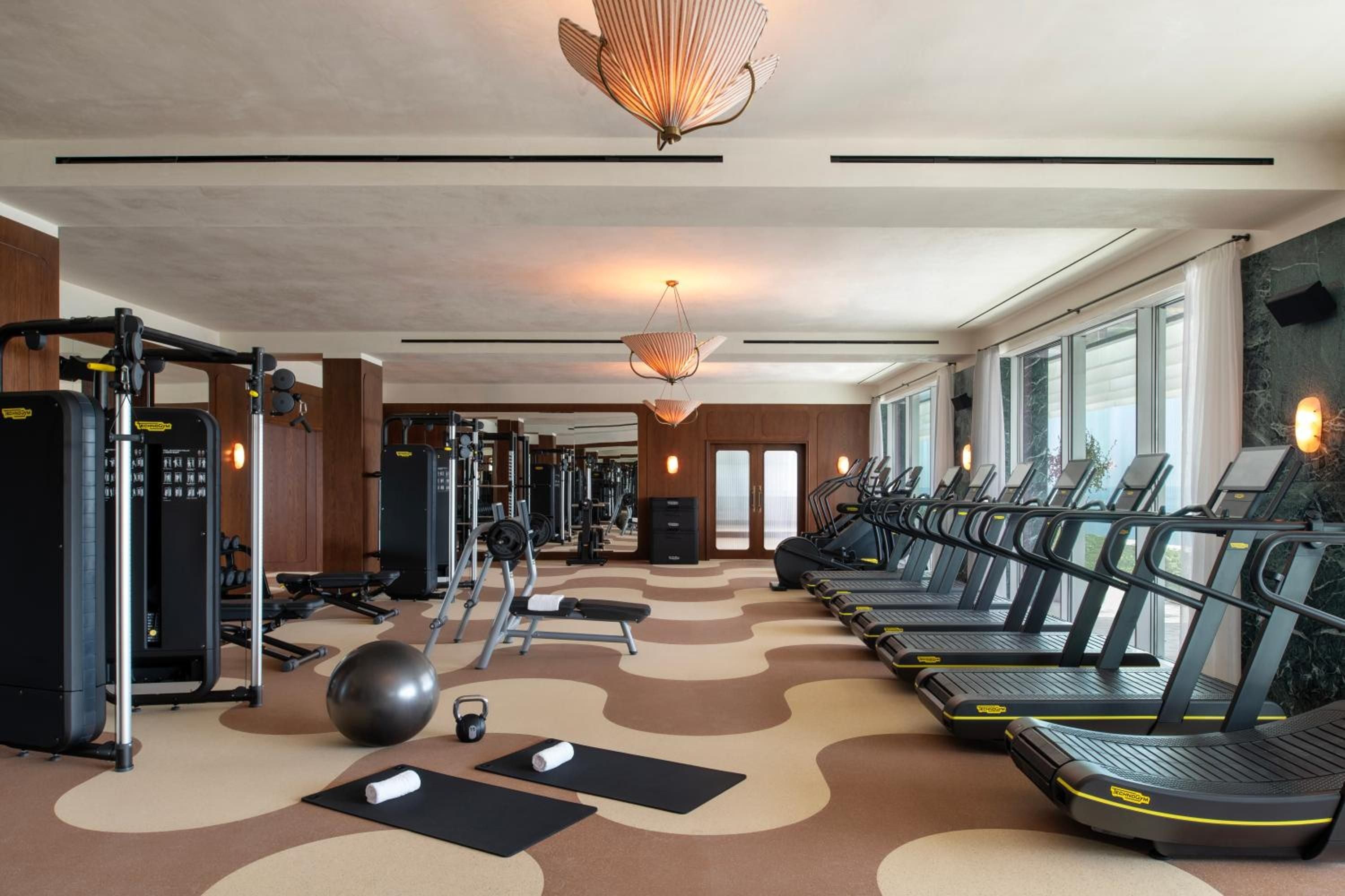 Curved terracotta flooring flows beneath state-of-the-art cardio equipment while sculptural pendant lights cast a warm glow over this thoughtfully designed wellness sanctuary.