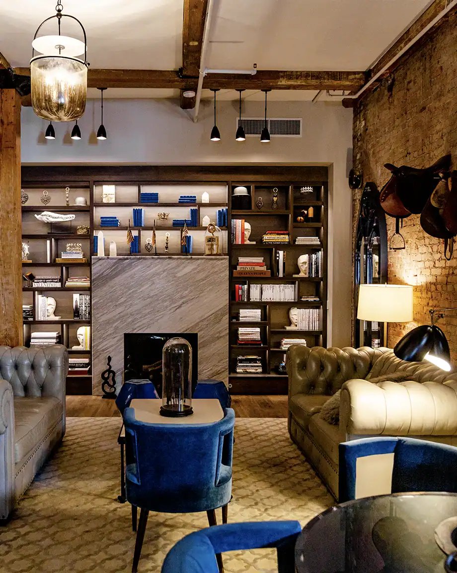 Exposed brick walls and weathered wooden beams frame sumptuous blue velvet seating, while equestrian saddles hint at the property's storied past in this sophisticated common area.