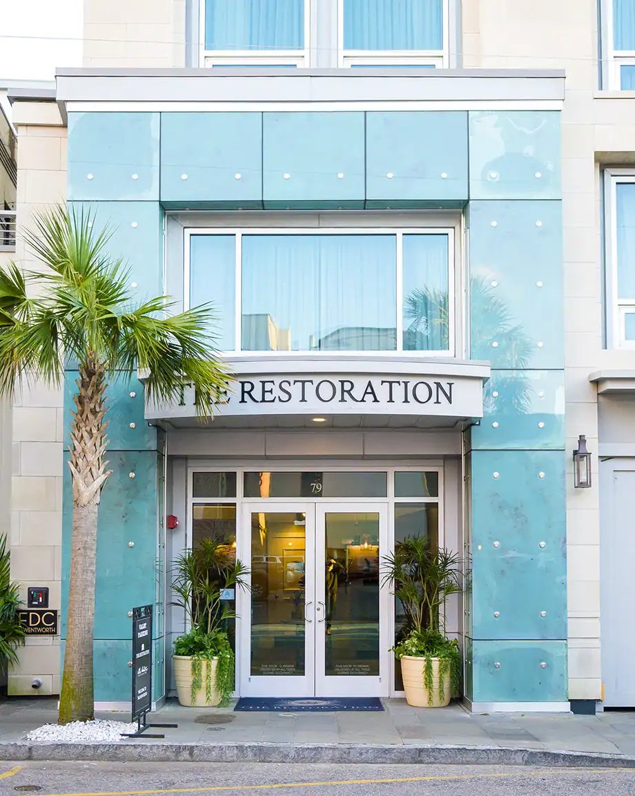 Turquoise paneling dotted with brass studs creates a striking coastal facade, while palm trees frame the welcoming glass entrance of this contemporary retreat.