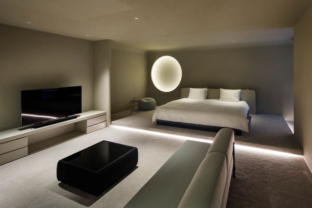 Ambient lighting bathes minimalist furnishings in warm honey tones, while a glowing circular sconce creates an intimate cocoon above the platform bed.