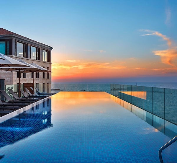 Infinity waters merge with ocean horizon as golden hour paints the sky, while sleek glass barriers frame this spectacular rooftop sanctuary above Miami Beach.