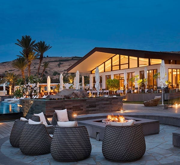 Desert-chic fire pit seating frames this modernist poolside retreat, where woven chairs invite lingering beneath starlit skies and palm silhouettes.