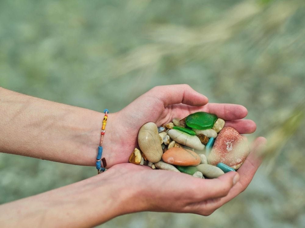 Cupped hands cradle smooth sea glass and weathered stones collected from Crete's pristine shores, each piece a natural souvenir polished by Mediterranean waves.