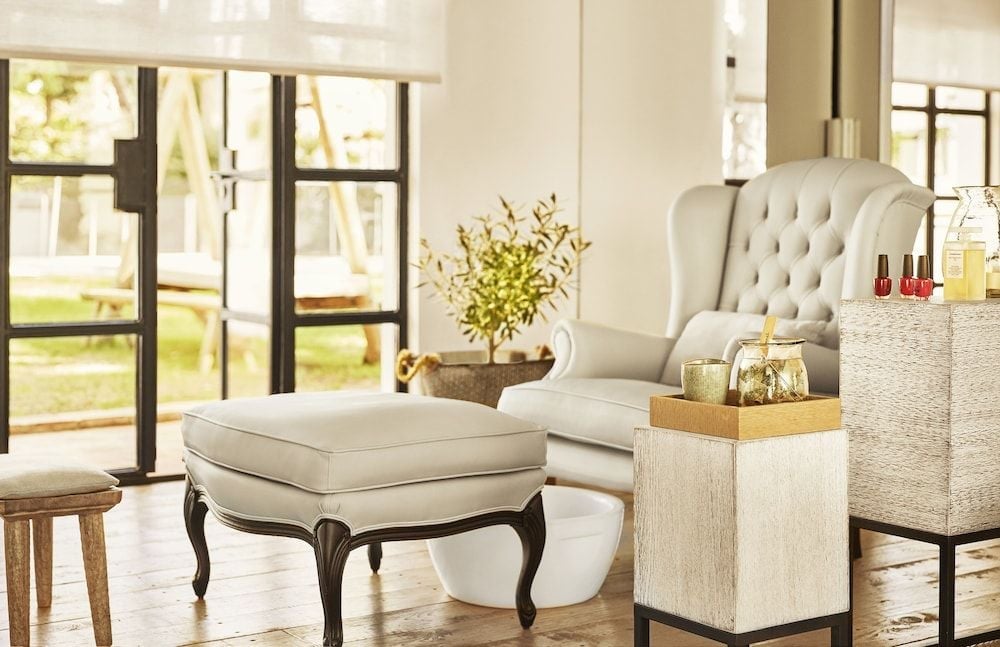 Cream leather wingback chairs and weathered wood textures create an inviting retreat where golden afternoon light streams through industrial-style windows, perfect for savoring Spanish aperitifs.