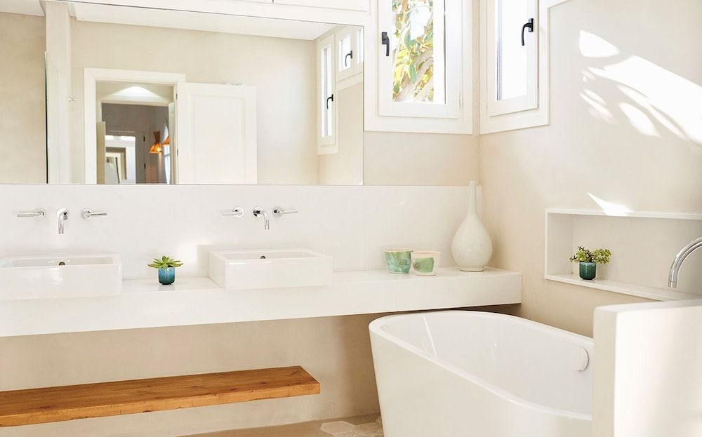 Sunlight streams through skylights onto polished white surfaces where dual vanities and a sculptural soaking tub create a serene spa-like sanctuary.