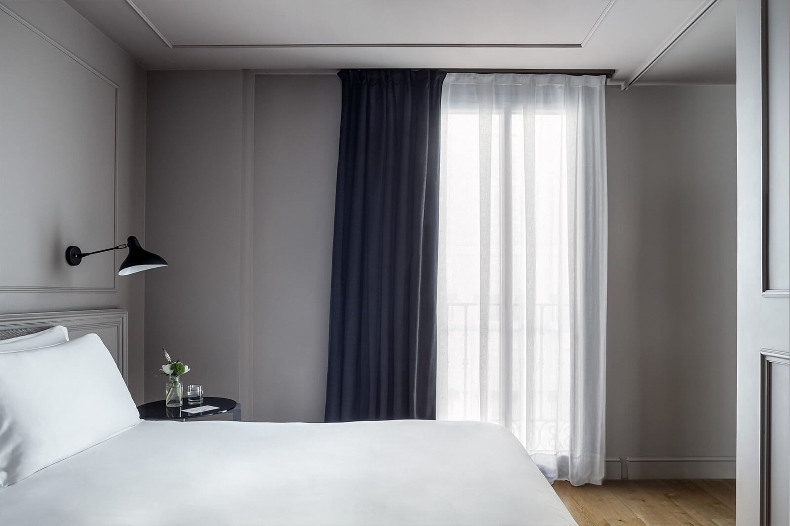Crisp white linens contrast beautifully against dove-gray walls, while navy curtains frame natural light streaming through sheer panels in this thoughtfully appointed guest room.