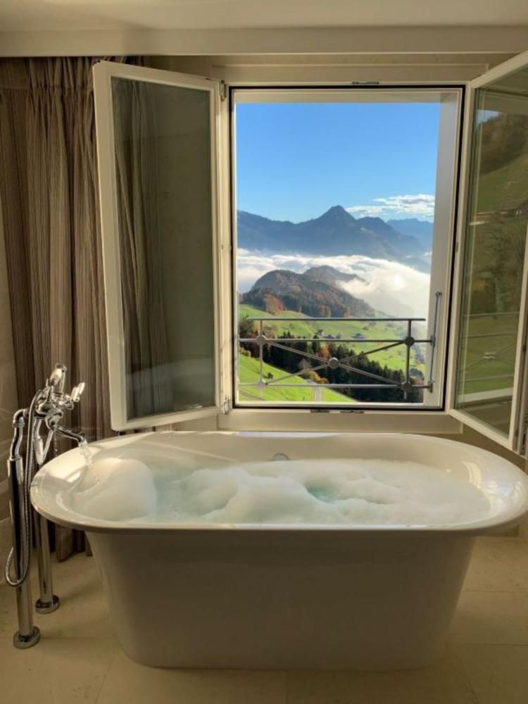 Alpine peaks float beyond clouds as steam rises from the marble soaking tub, where floor-to-ceiling windows frame Switzerland's dramatic mountain theater in perfect solitude.