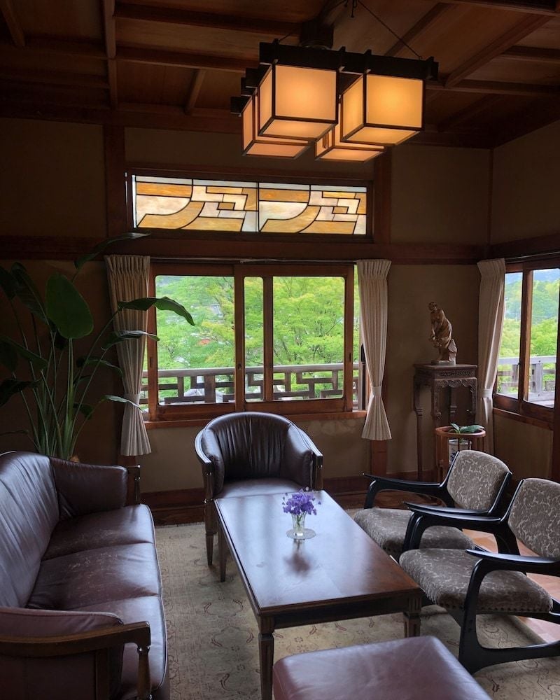 Warm lantern light illuminates traditional seating where stained glass windows frame verdant mountain views, creating an intimate sanctuary above Kyoto's ancient temples.