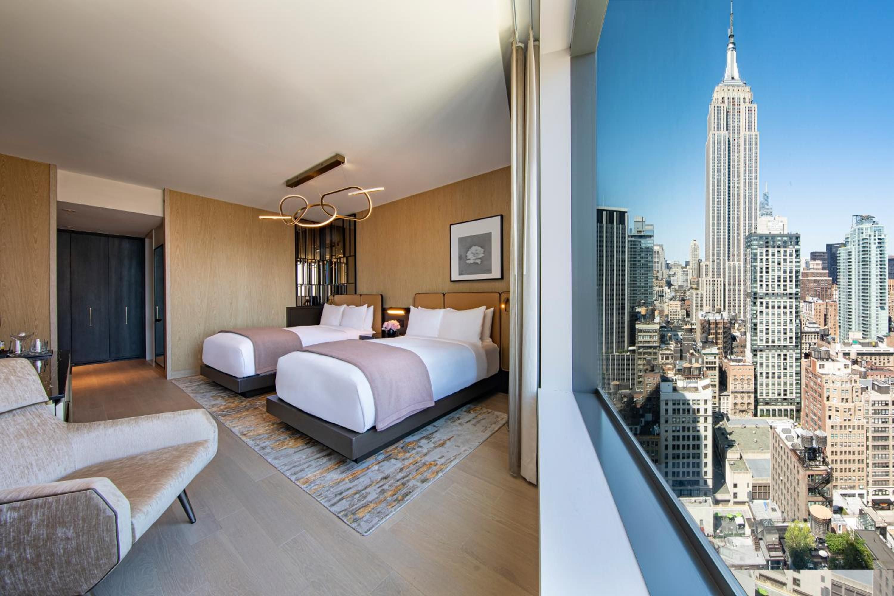 Floor-to-ceiling windows frame the Empire State Building from this sophisticated suite, where warm wood tones and contemporary furnishings create an elevated Manhattan sanctuary.
