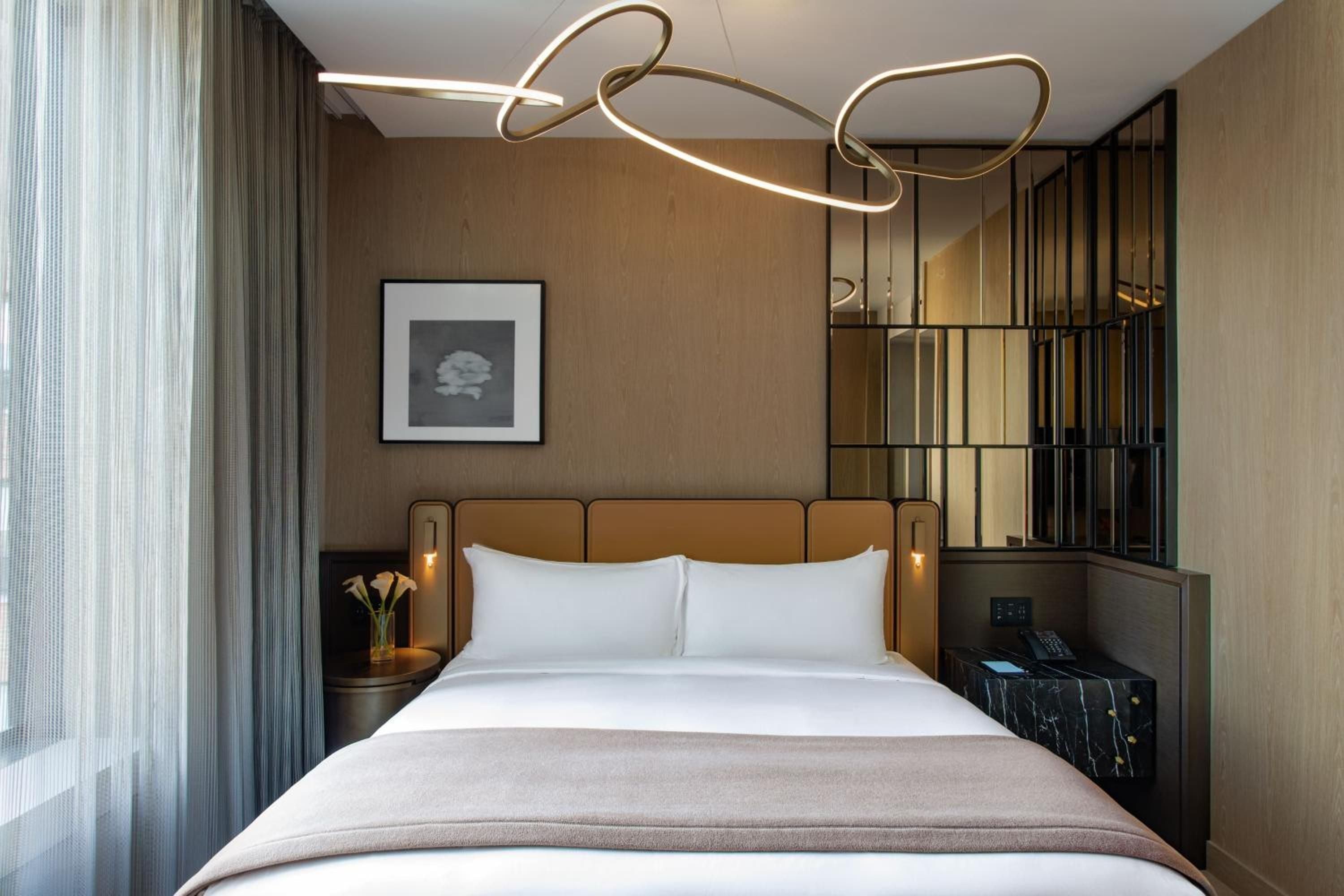 Sculptural lighting ribbons dance above cognac leather headboards, while floor-to-ceiling windows bathe warm wood tones in Manhattan's golden hour glow.