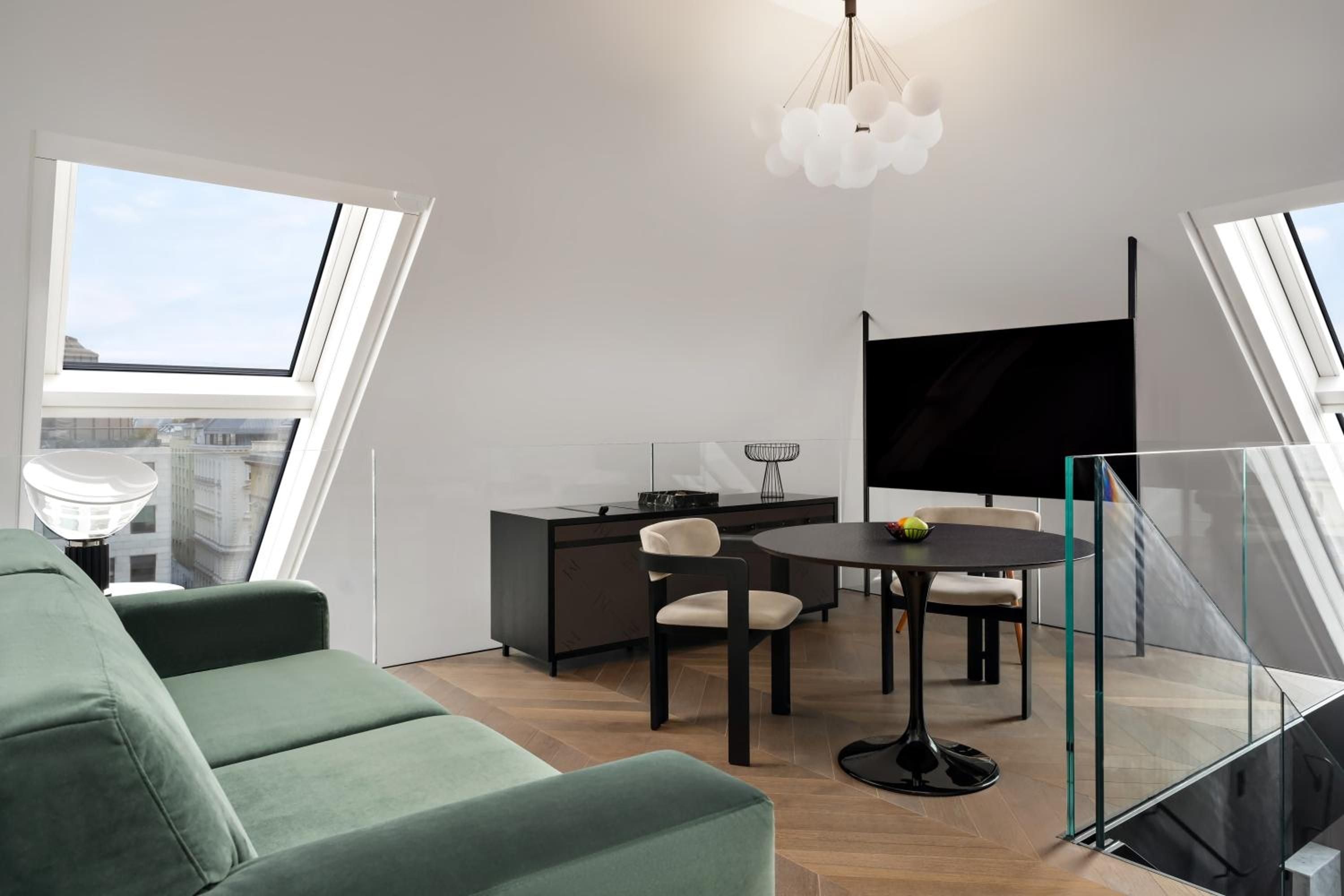 Skylights flood this penthouse suite with natural light, where emerald velvet seating and sleek dining furniture create an intimate Vienna retreat above the city's rooftops.