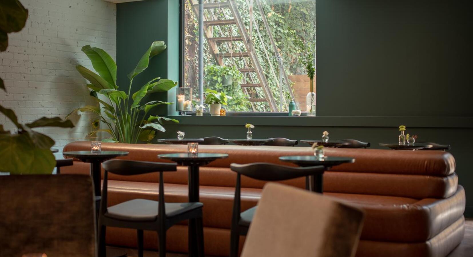 Curved cognac banquettes embrace intimate tables where natural light filters through verdant garden views, creating The Annex's signature warmth.
