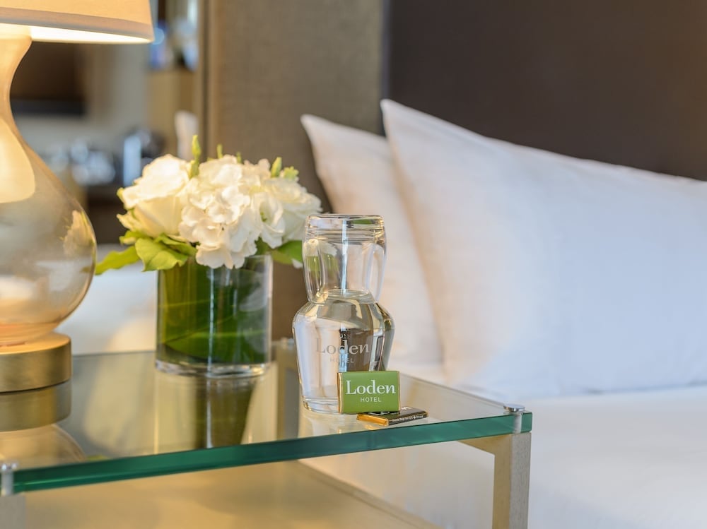 Crisp white linens meet thoughtful touches like fresh blooms and glass water carafes on sleek bedside tables, creating an atmosphere of understated luxury.