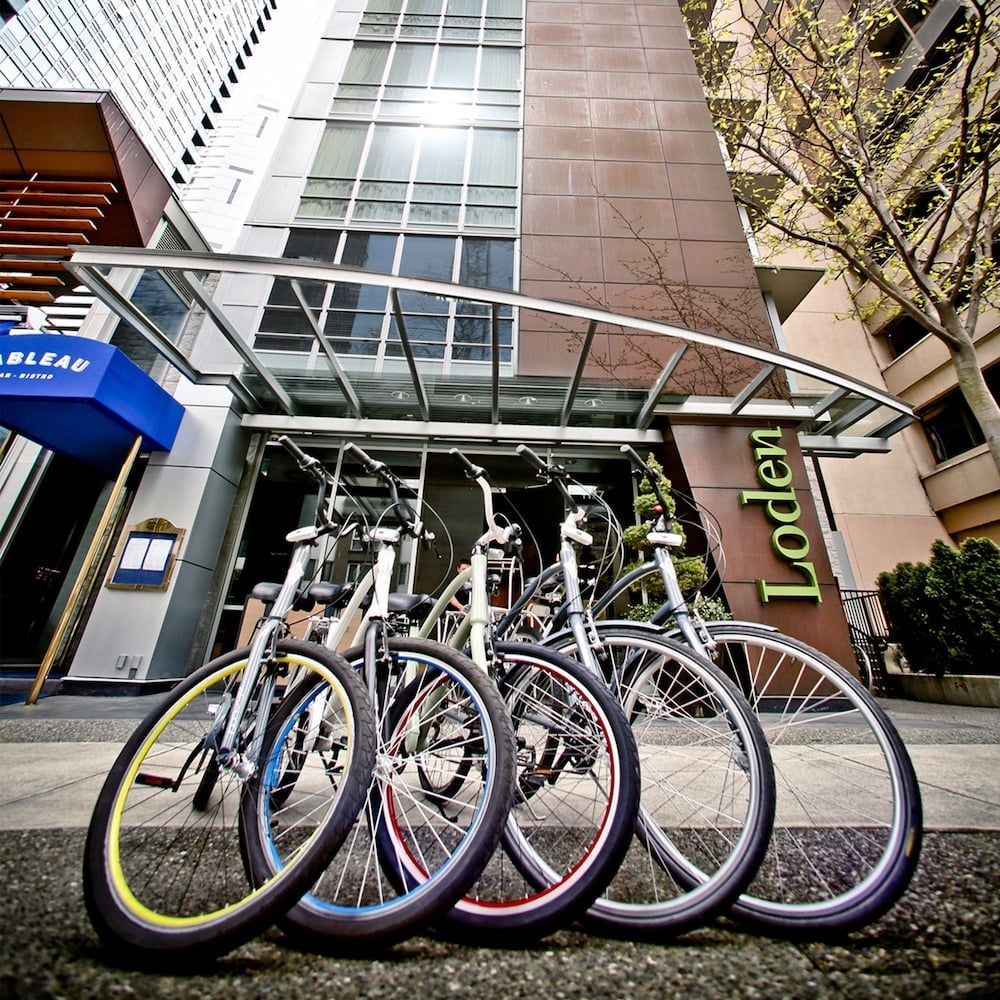 Colorful bicycles line the sidewalk outside Loden's modern glass entrance, inviting guests to explore Vancouver's walkable neighborhoods with eco-friendly style.