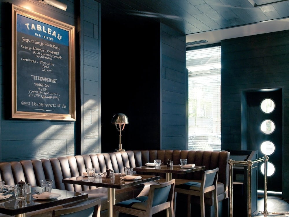 Tableau's moody blue banquettes and warm brass accents create an intimate dining atmosphere, where chalkboard specials and golden table lamps invite lingering conversations over craft cocktails.