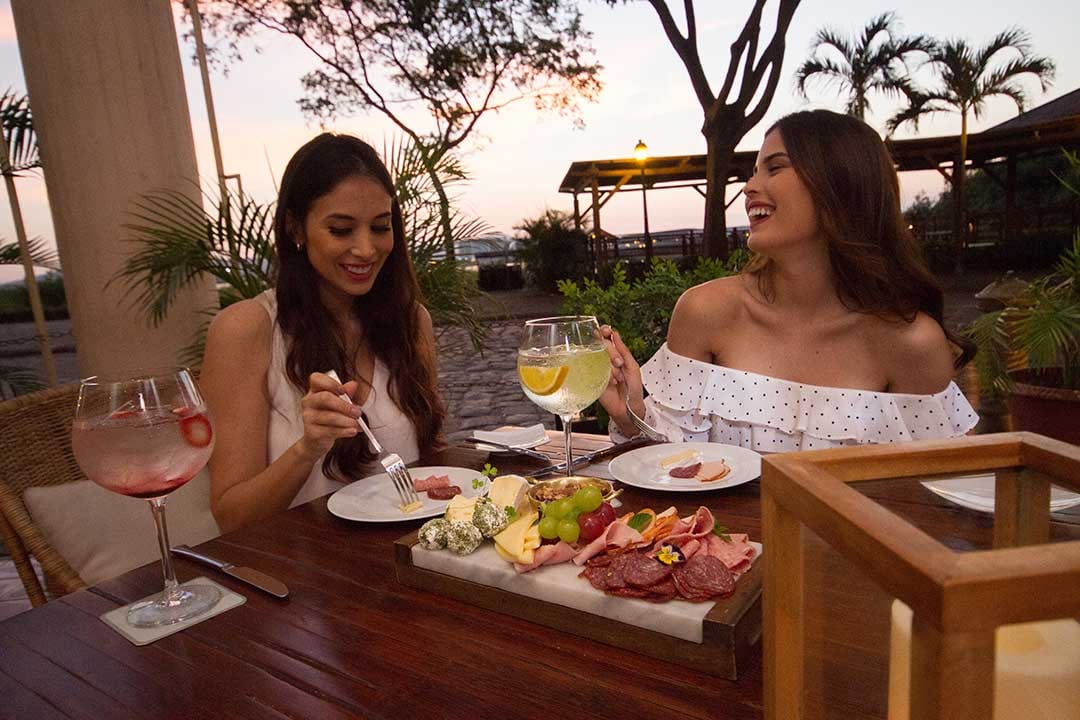 Golden hour transforms the rooftop terrace into an intimate dining sanctuary, where charcuterie boards and wine glasses catch the last light filtering through swaying palms.
