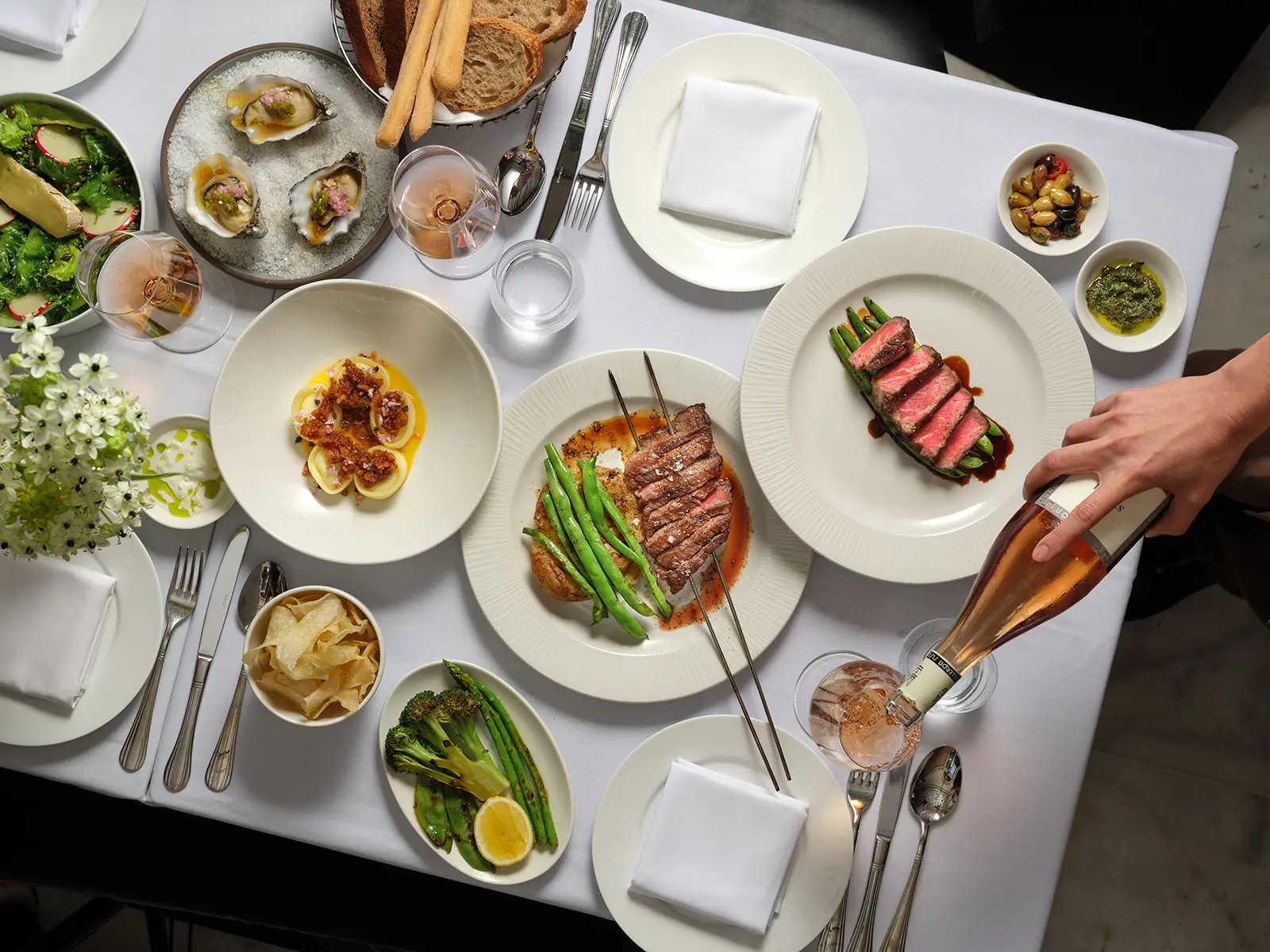 Champagne flows as perfectly seared steaks and fresh oysters transform dinner into an elegant affair, with asparagus spears and artisanal accompaniments completing the sophisticated spread.