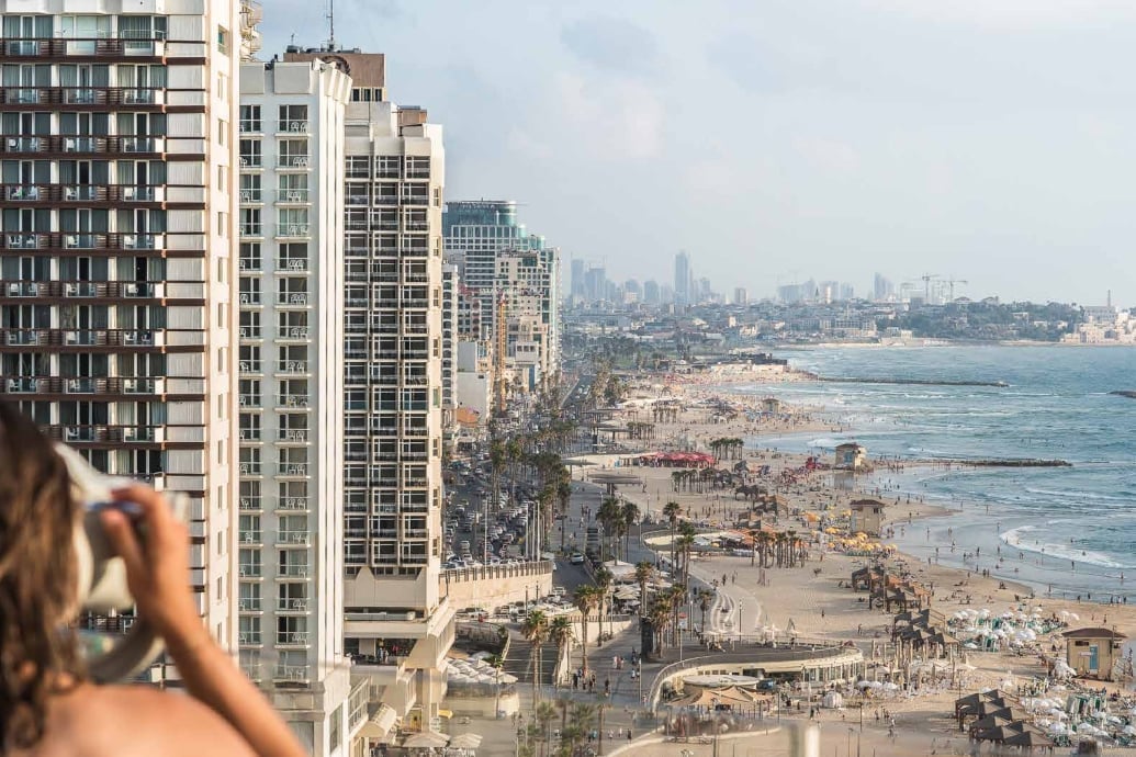 From a high-floor balcony, Tel Aviv's golden coastline unfolds in perfect panorama—modern towers giving way to endless Mediterranean beaches dotted with umbrellas and life.