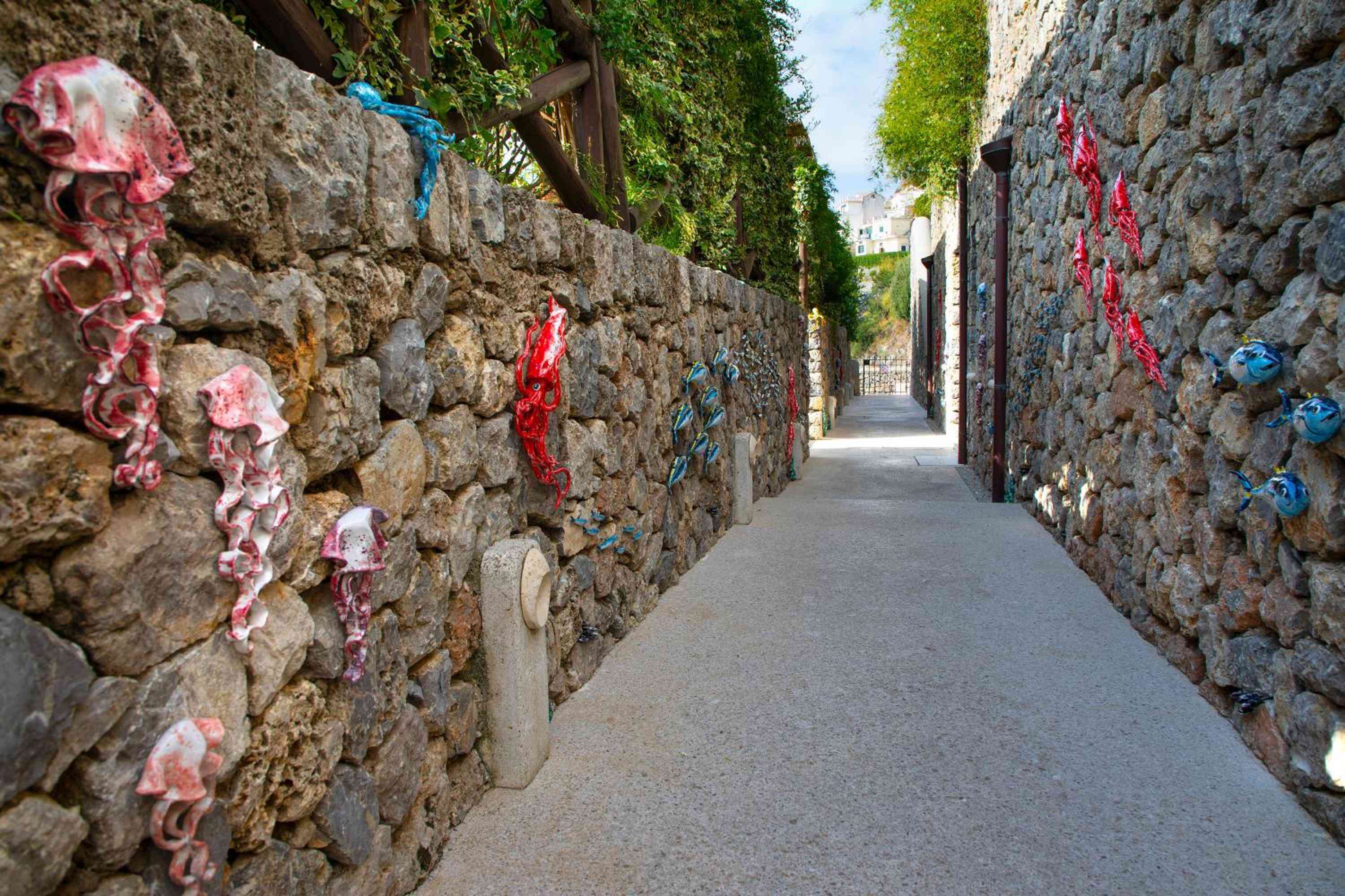 Colorful ribbons flutter against ancient stone walls along garden pathways, where centuries-old architecture meets whimsical artistic touches in this cliffside sanctuary.