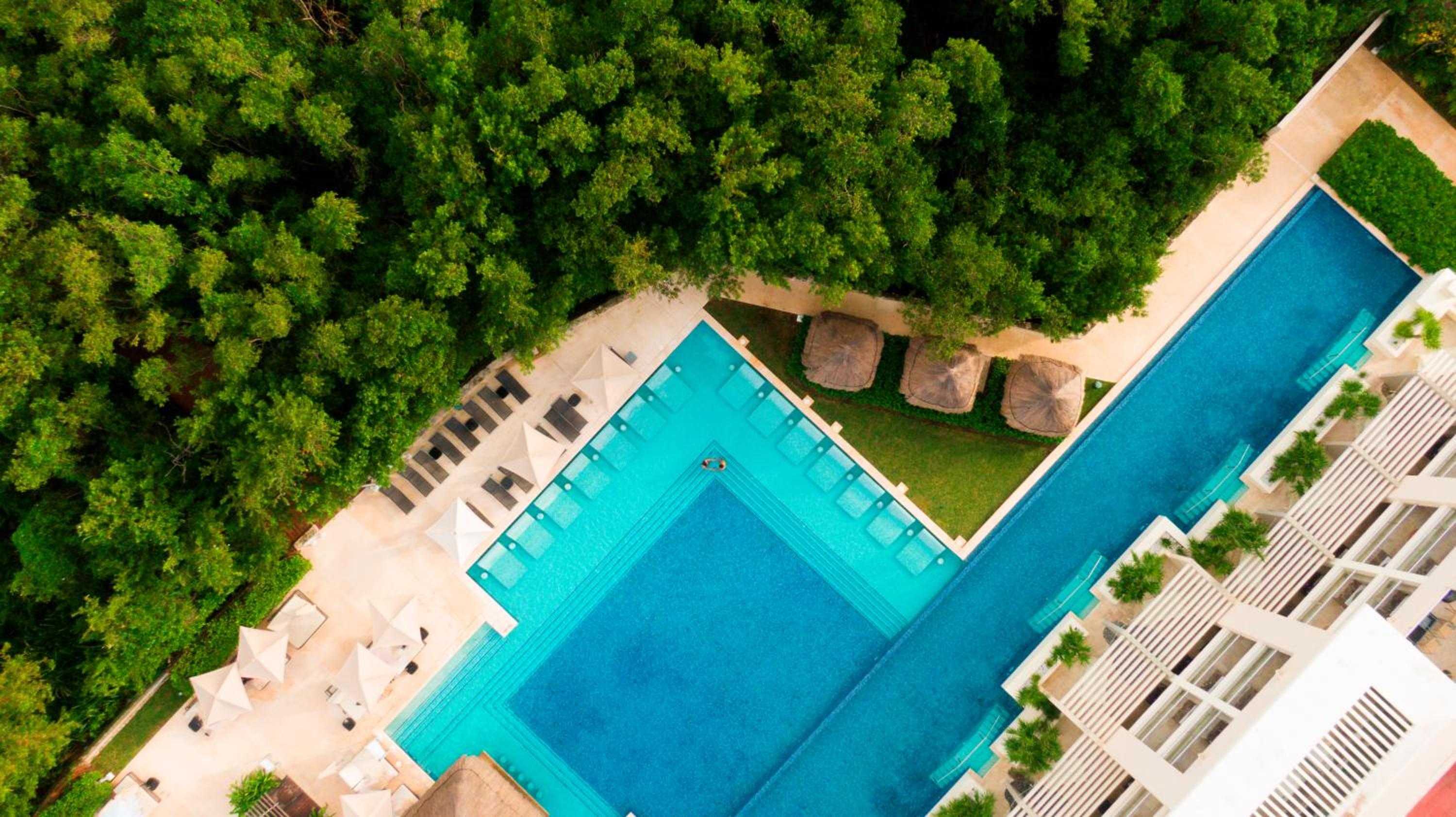 Turquoise waters create geometric perfection in this L-shaped infinity pool complex, where tropical forest meets meticulously designed leisure spaces dotted with traditional palapas.