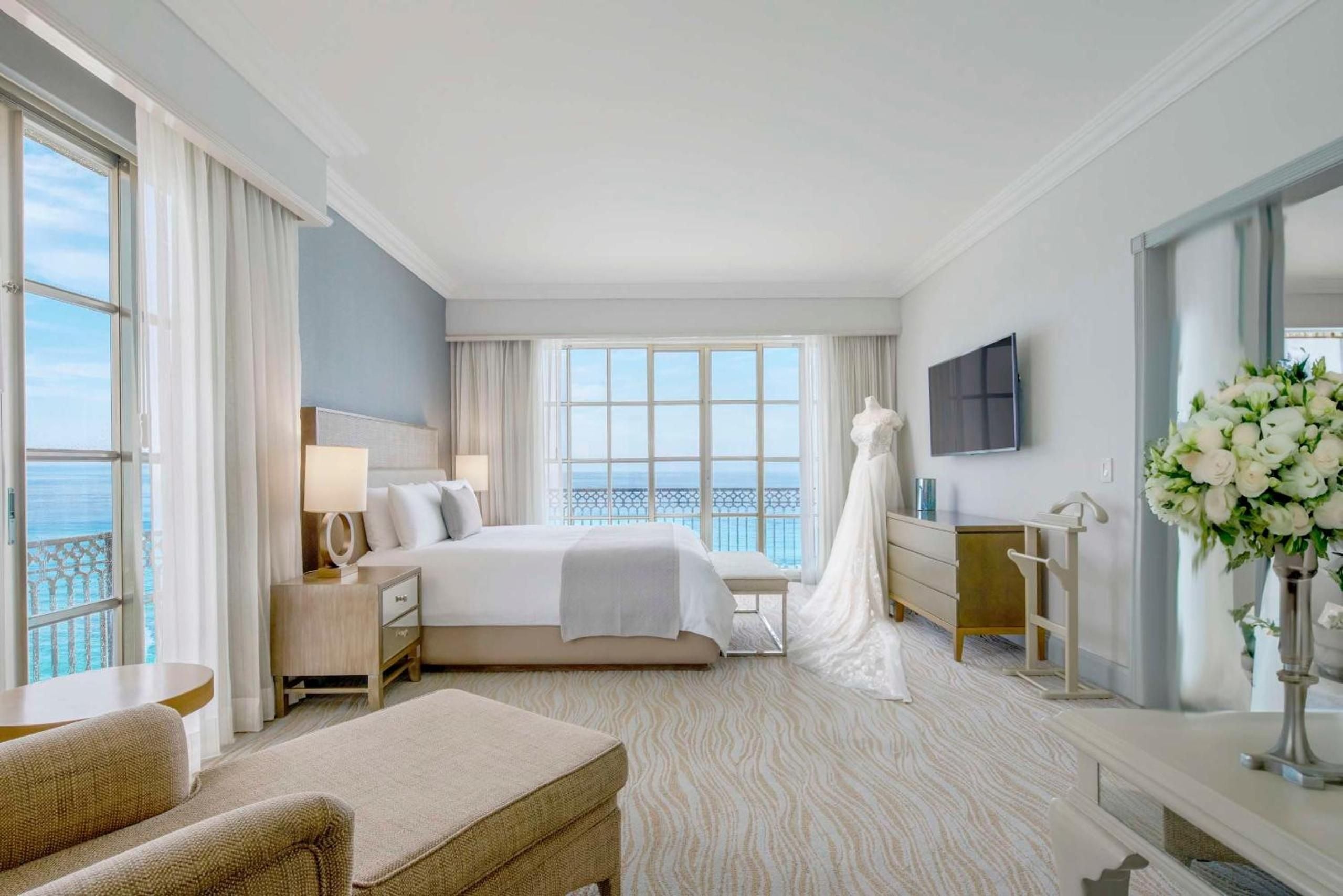 Crisp white linens and warm wood furnishings create a serene sanctuary, where floor-to-ceiling windows frame endless Caribbean blues beyond the private balcony.