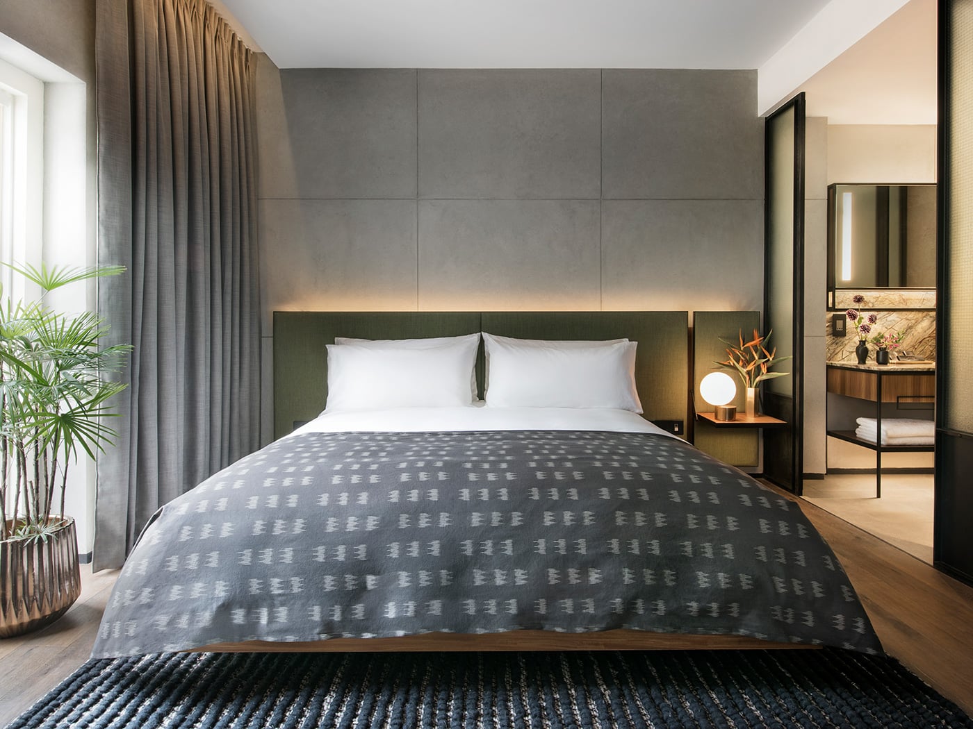 Charcoal-gray headboard walls and warm wood tones create an intimate cocoon, where industrial heritage meets contemporary comfort in this thoughtfully designed guest room.