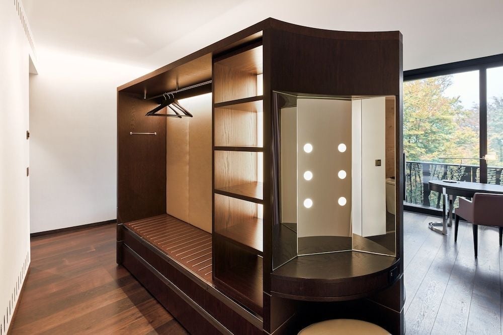 Rich walnut cabinetry conceals a sophisticated dressing area where warm LED lighting illuminates custom shelving and a sleek glass-enclosed vanity space.