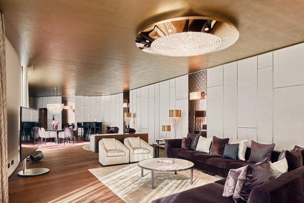 Curved walls and warm metallic ceilings create an intimate conversation area where plush purple sectionals invite lingering over cocktails in sophisticated comfort.