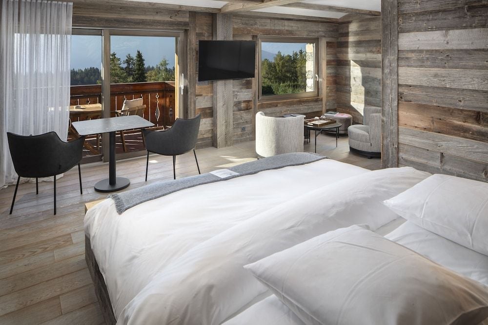 Reclaimed wood beams and pristine white linens create alpine sophistication in this mountain suite, where floor-to-ceiling windows frame evergreen vistas beyond the private balcony.