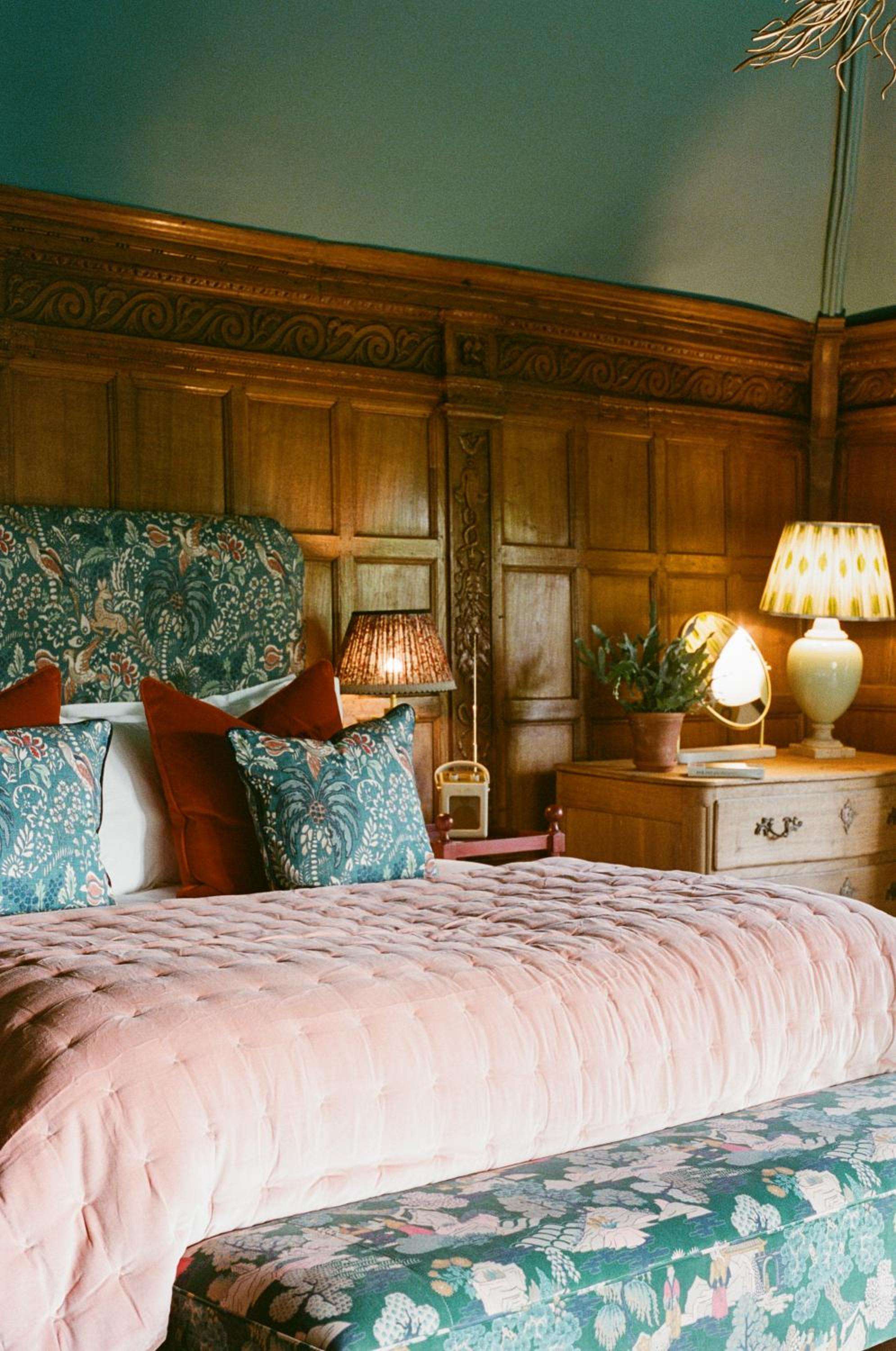 Rich wood paneling frames botanical-patterned linens in salmon and teal, where warm lamplight creates an intimate sanctuary steeped in country house charm.