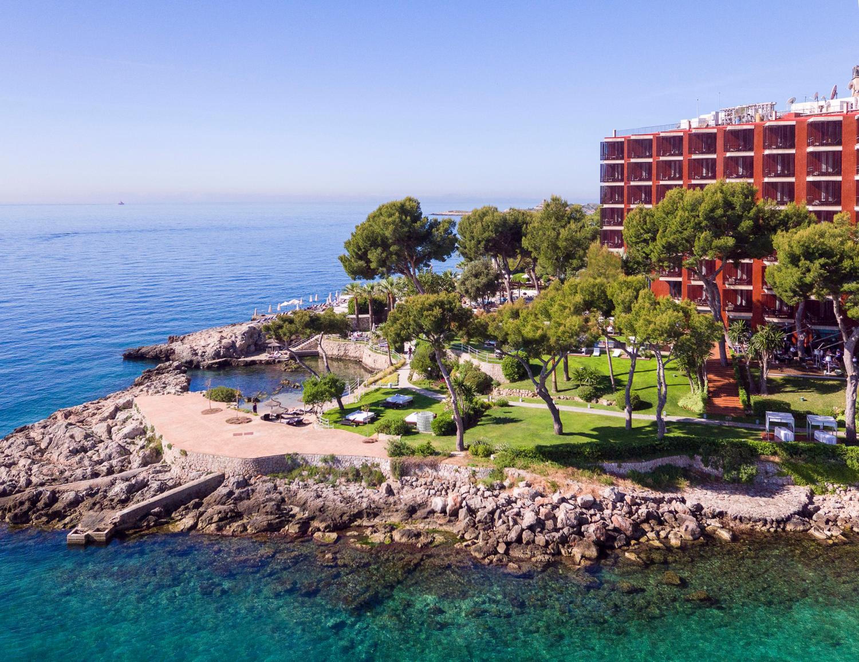 Crystalline Mediterranean waters lap against rocky coves where manicured gardens meet the sea, creating an intimate coastal sanctuary beneath endless azure skies.