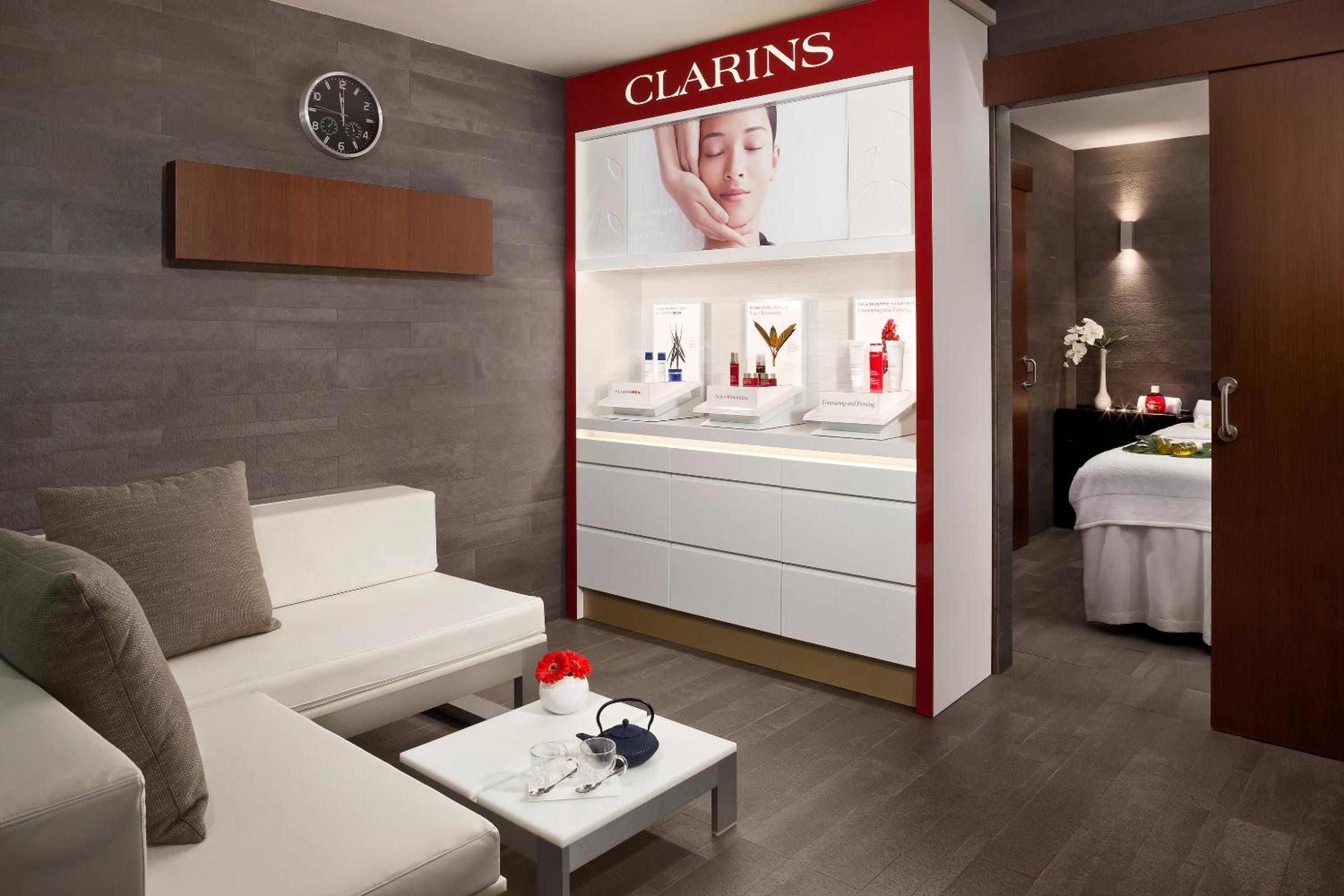 Clarins products gleam beneath soft lighting in this serene treatment suite, where contemporary design meets wellness luxury through sleek cabinetry and plush seating.