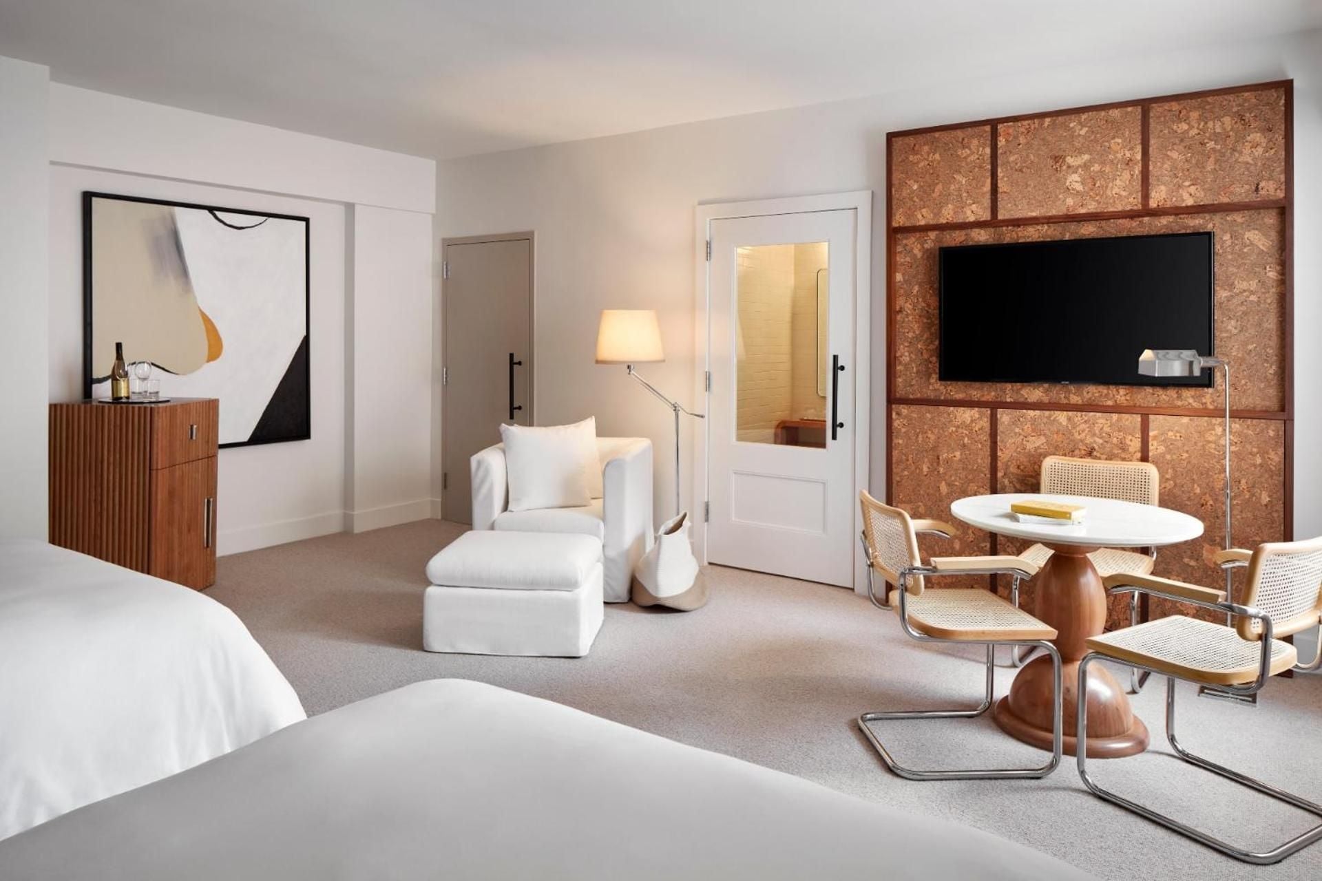 Cork-paneled walls create warmth in this sophisticated suite, where Breuer-style chairs and crisp white linens blend mid-century elegance with contemporary comfort.