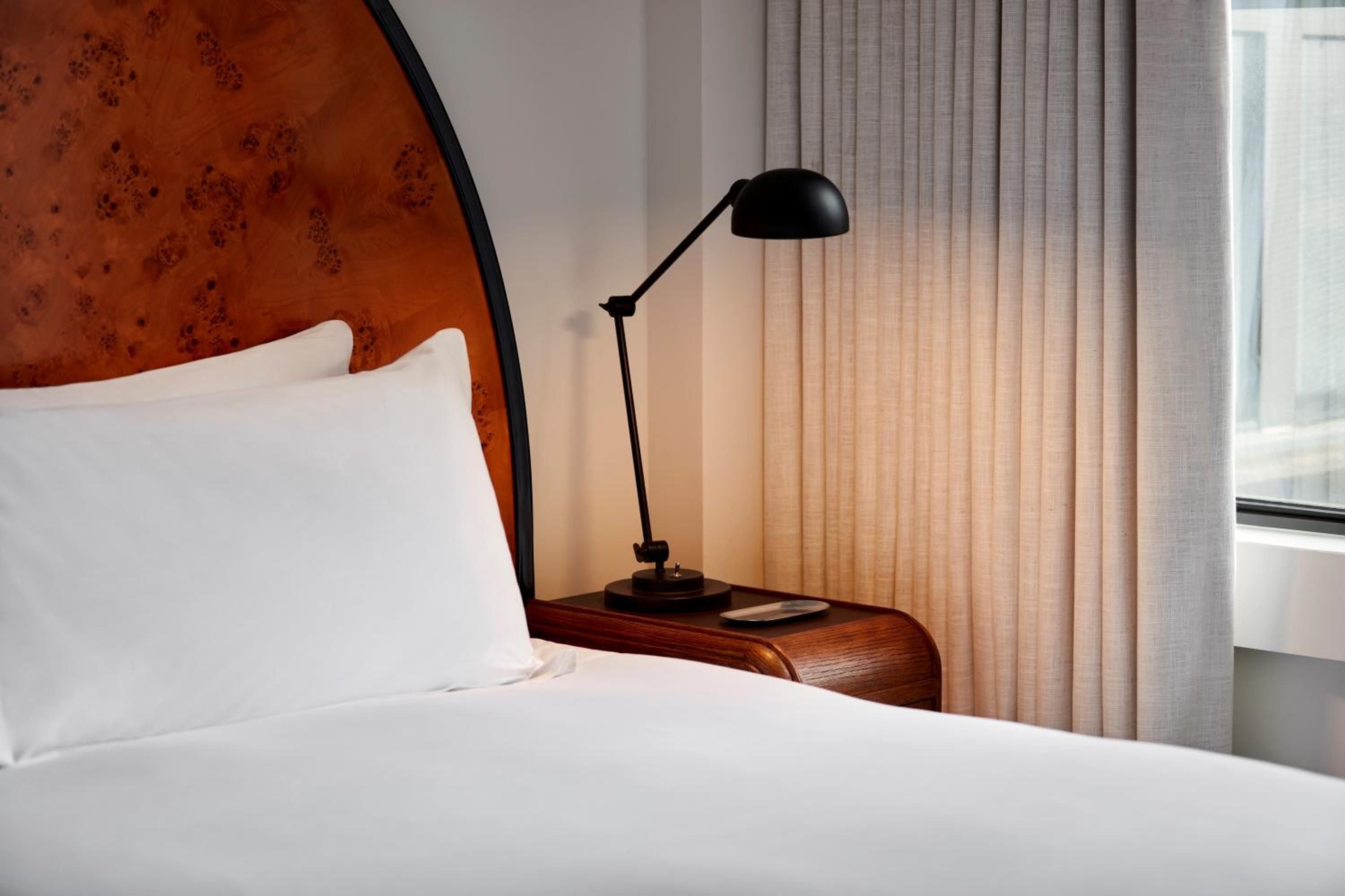 Warm rust-toned headboards with textured patina create intimate cocoons, while sleek task lighting and curved walnut nightstands add sophisticated functionality to each thoughtfully designed guest room.