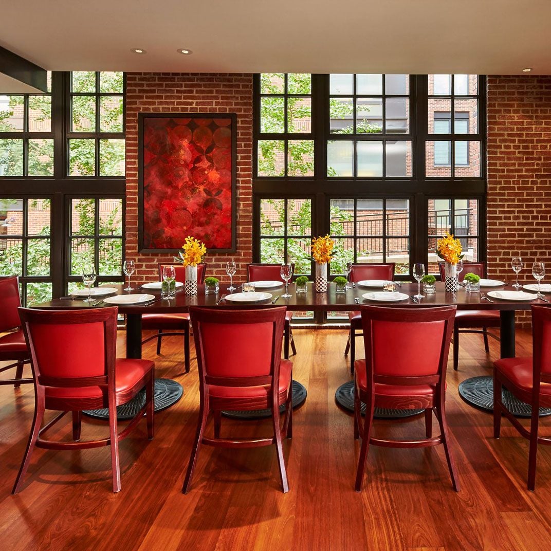 Crimson leather chairs and exposed brick walls create an intimate dining atmosphere, while floor-to-ceiling windows frame views of Georgetown's historic streetscape beyond.