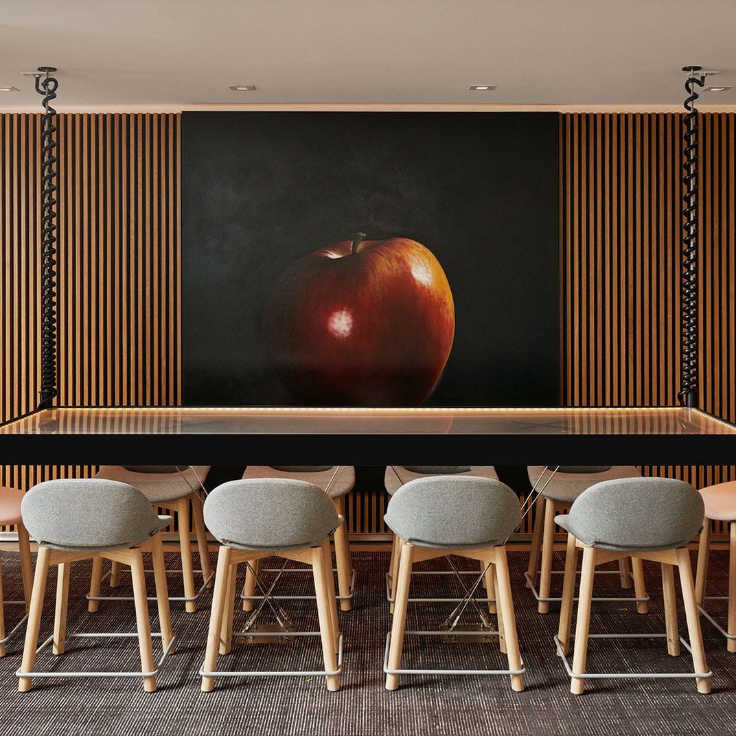 Bold artistic flair meets intimate dining as a dramatic red apple painting commands attention above sleek wooden slats and contemporary counter seating.