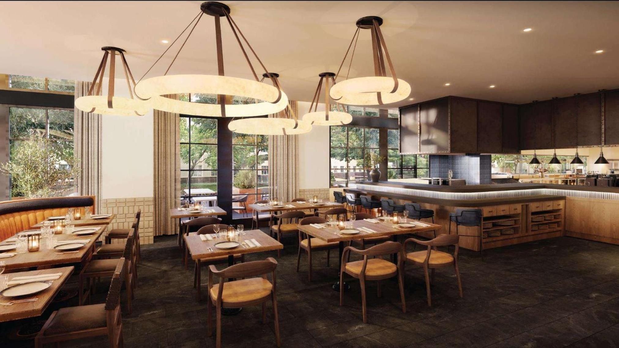 Warm pendant lights cast an inviting glow over natural wood tables and leather banquettes, while floor-to-ceiling windows flood the dining space with gentle daylight.